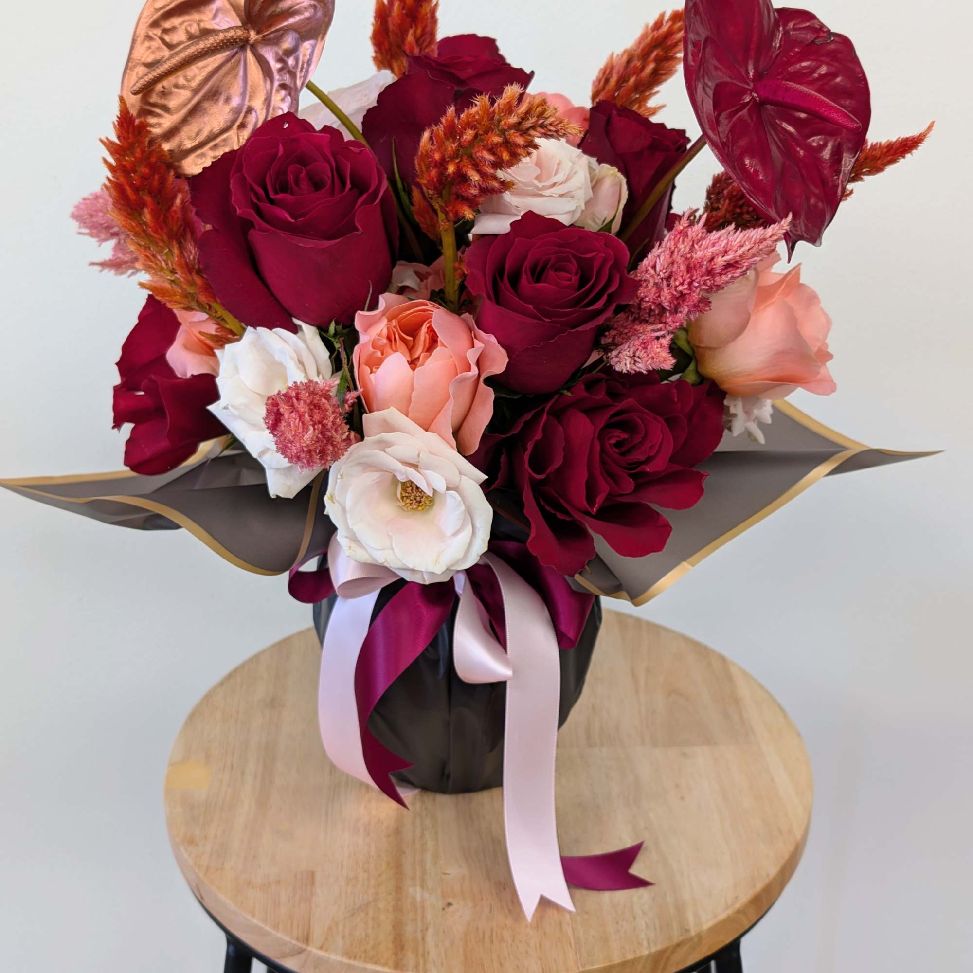 Bouquet of burgundy and blush roses with anthuriums in a black wrap