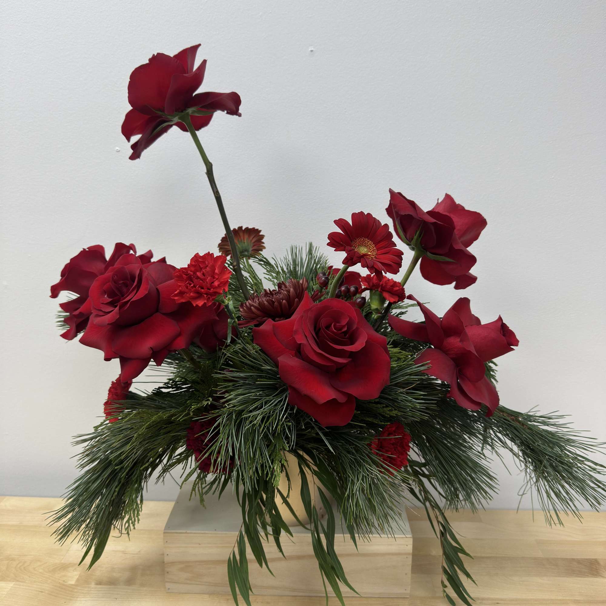 Red roses and mixed flowers in a low vase with pine greenery