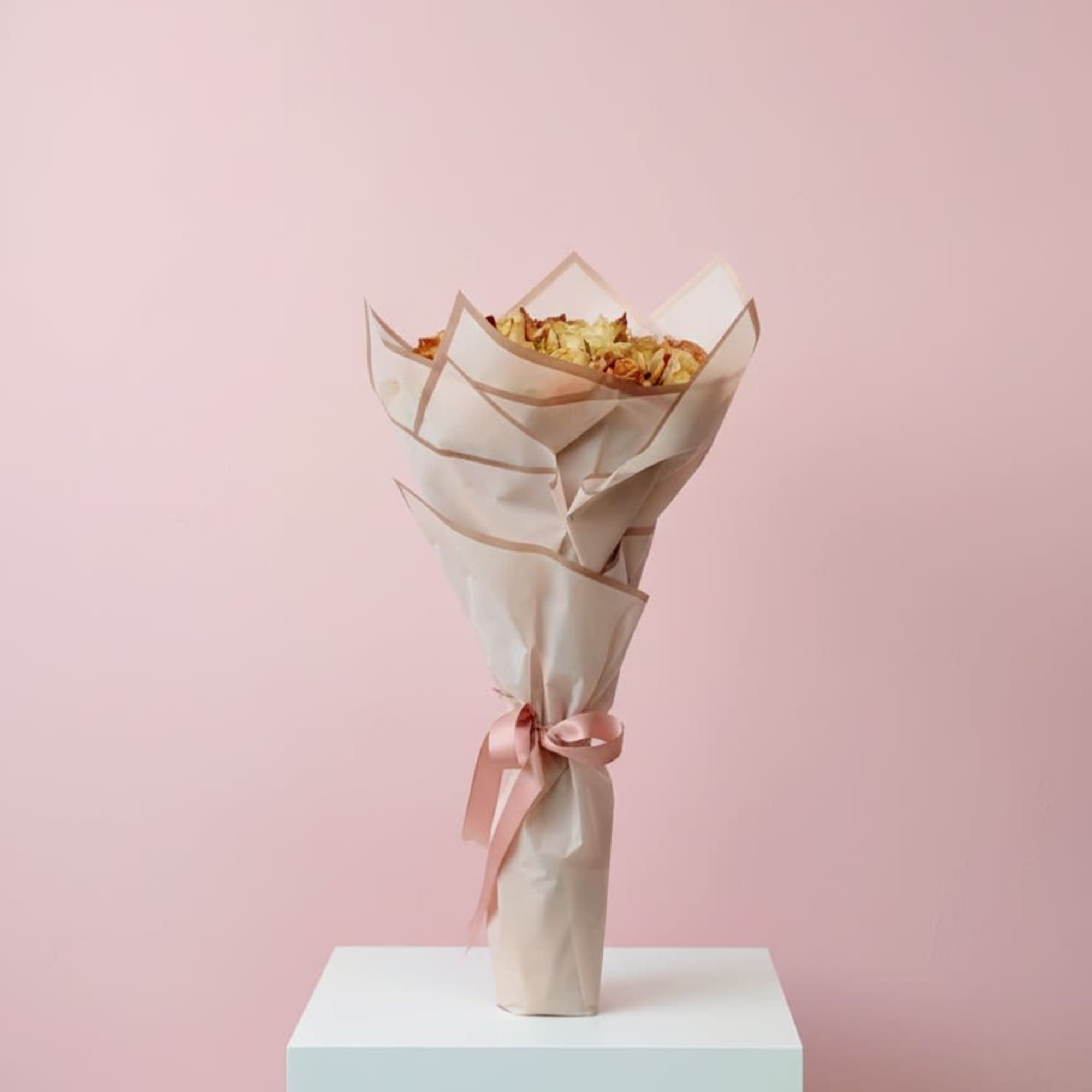 Wrapped bouquet with dried petals and a pink ribbon on a pedestal
