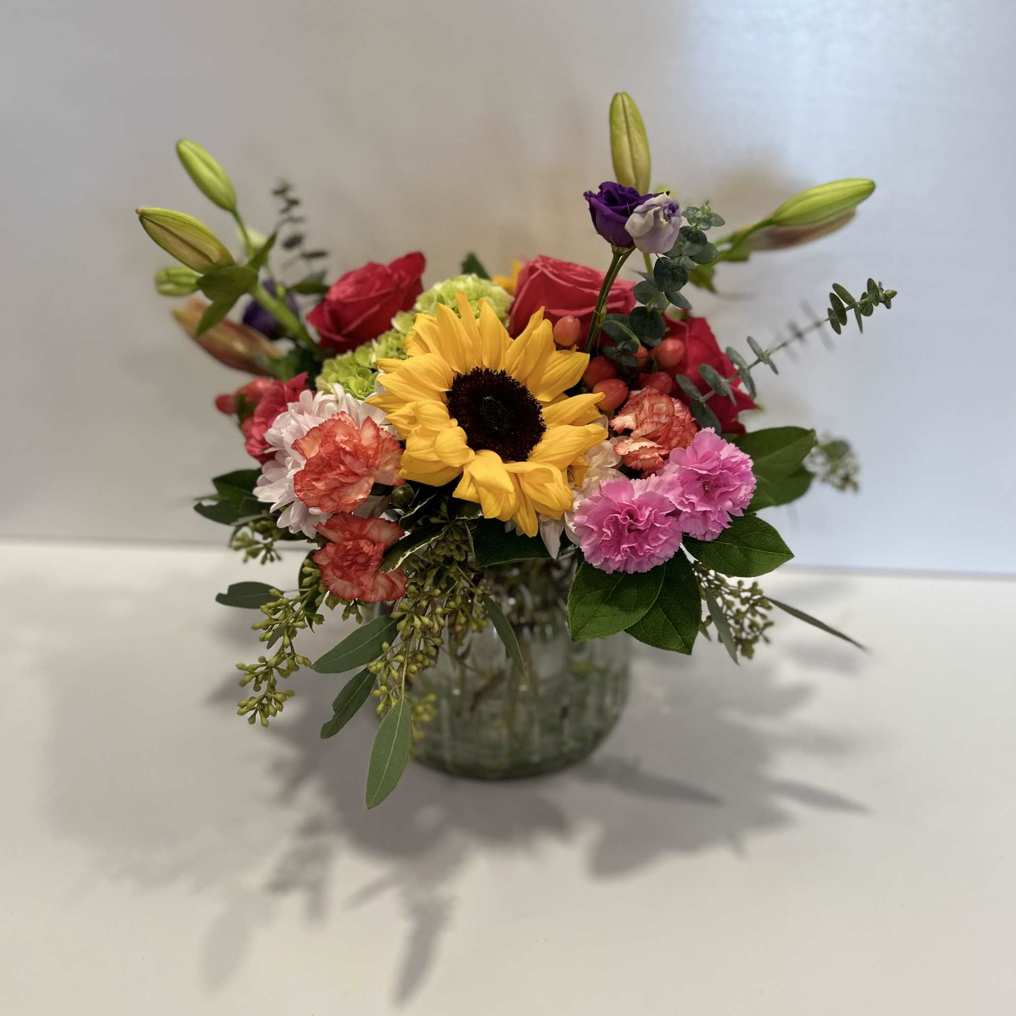 Mixed bouquet with a sunflower, roses, carnations, and lilies in a glass vase