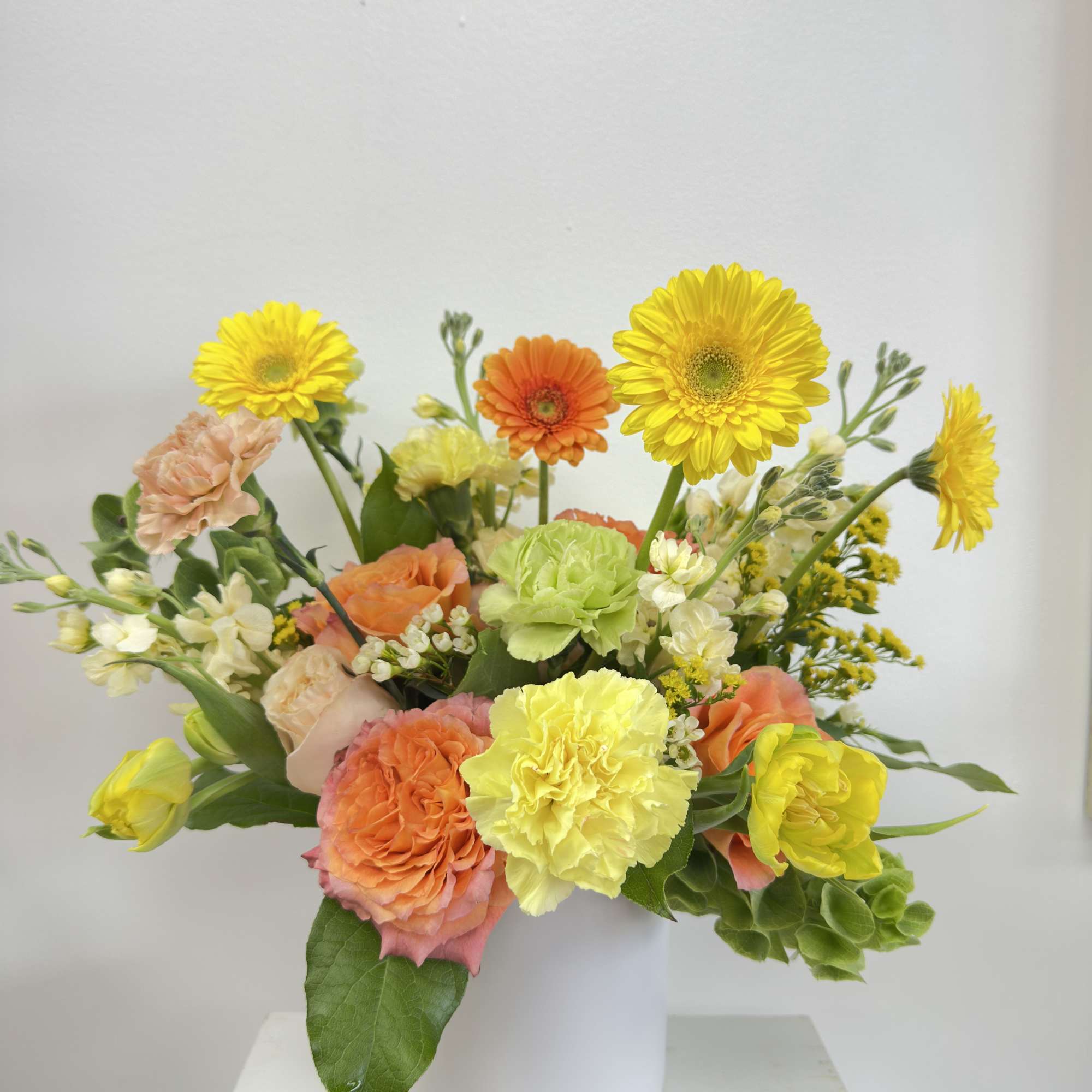 Cheerful arrangement of yellow gerbera daisies, orange roses, and carnations in a white vase