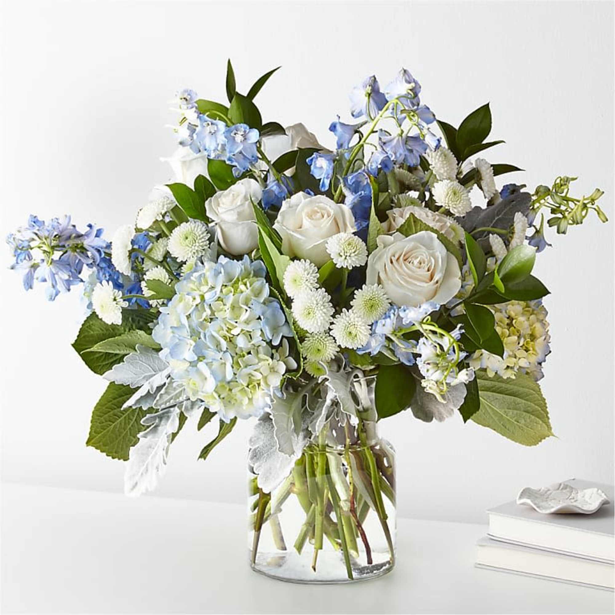 White roses and blue flowers arranged in a clear glass vase