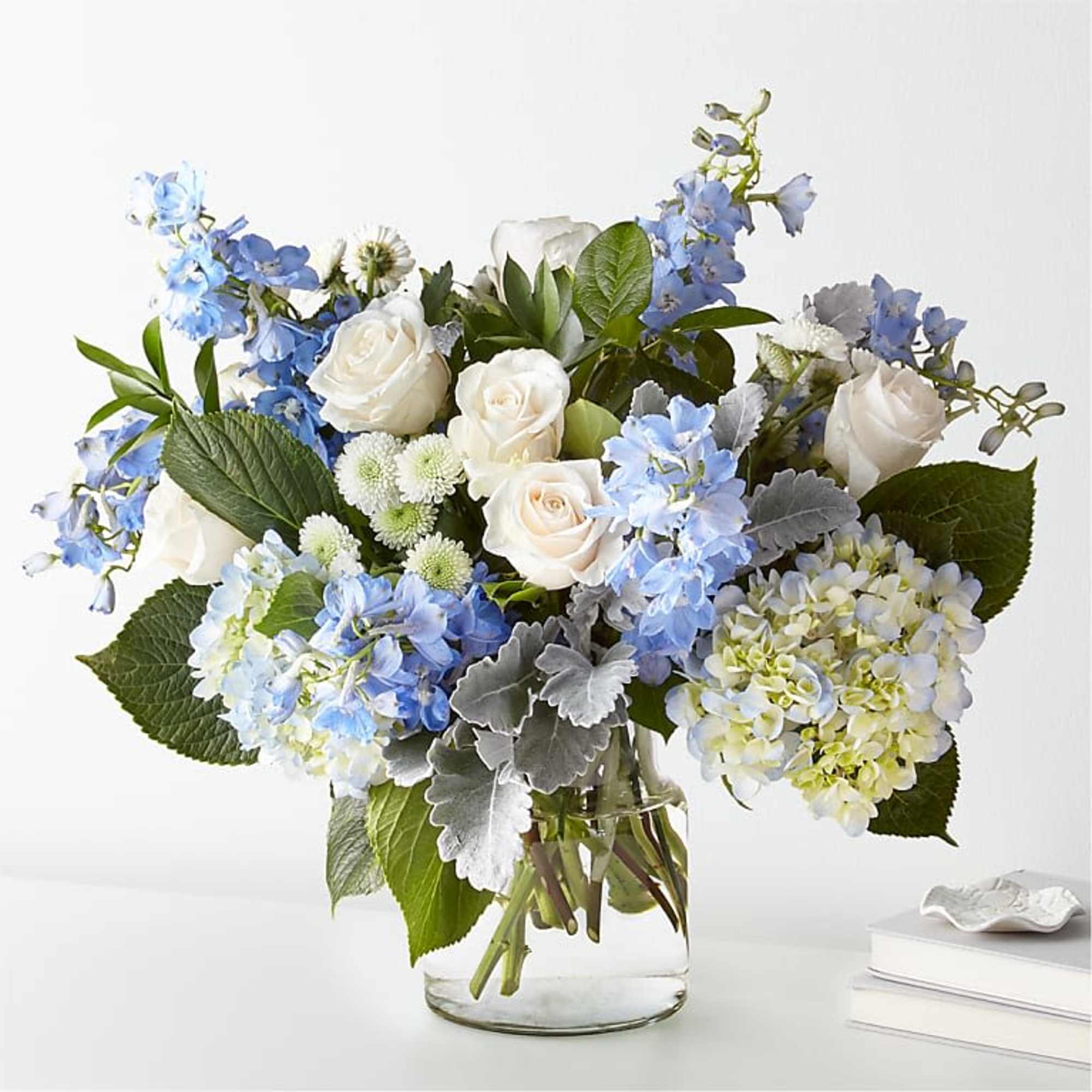 White roses and blue flowers arranged in a clear glass vase