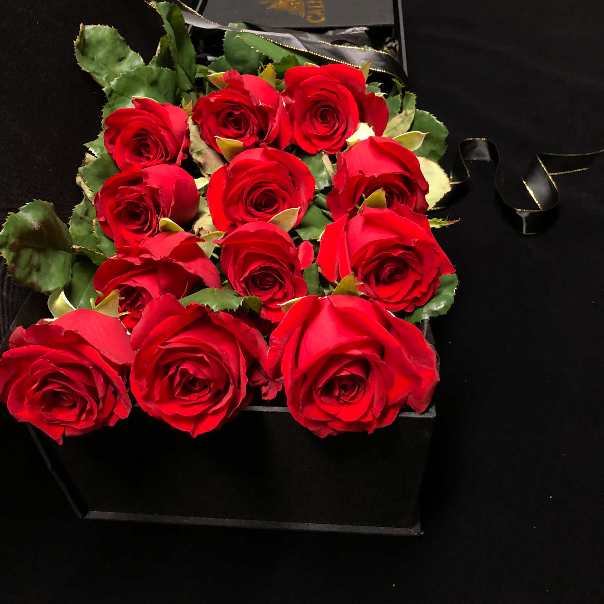 Box of red roses with green leaves on a black background