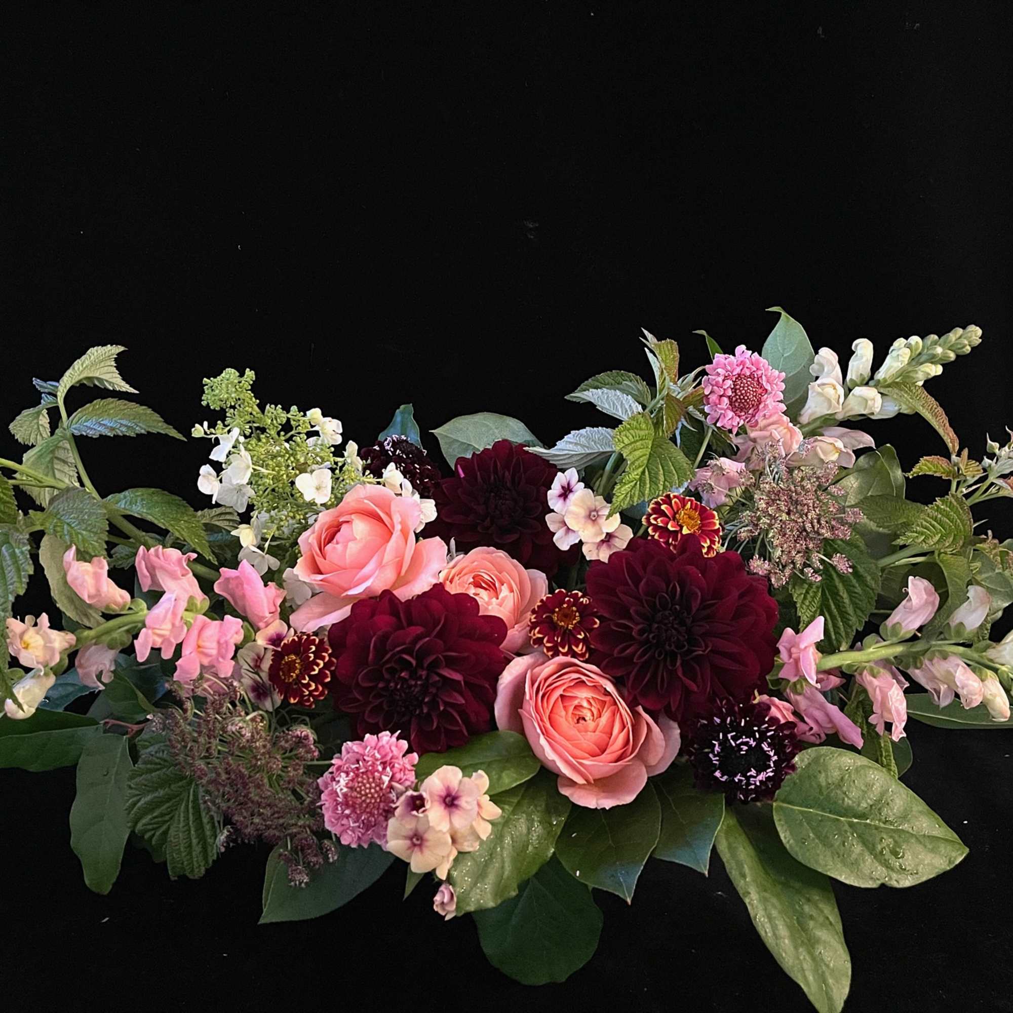 Low floral arrangement with pink and burgundy blooms on a black background