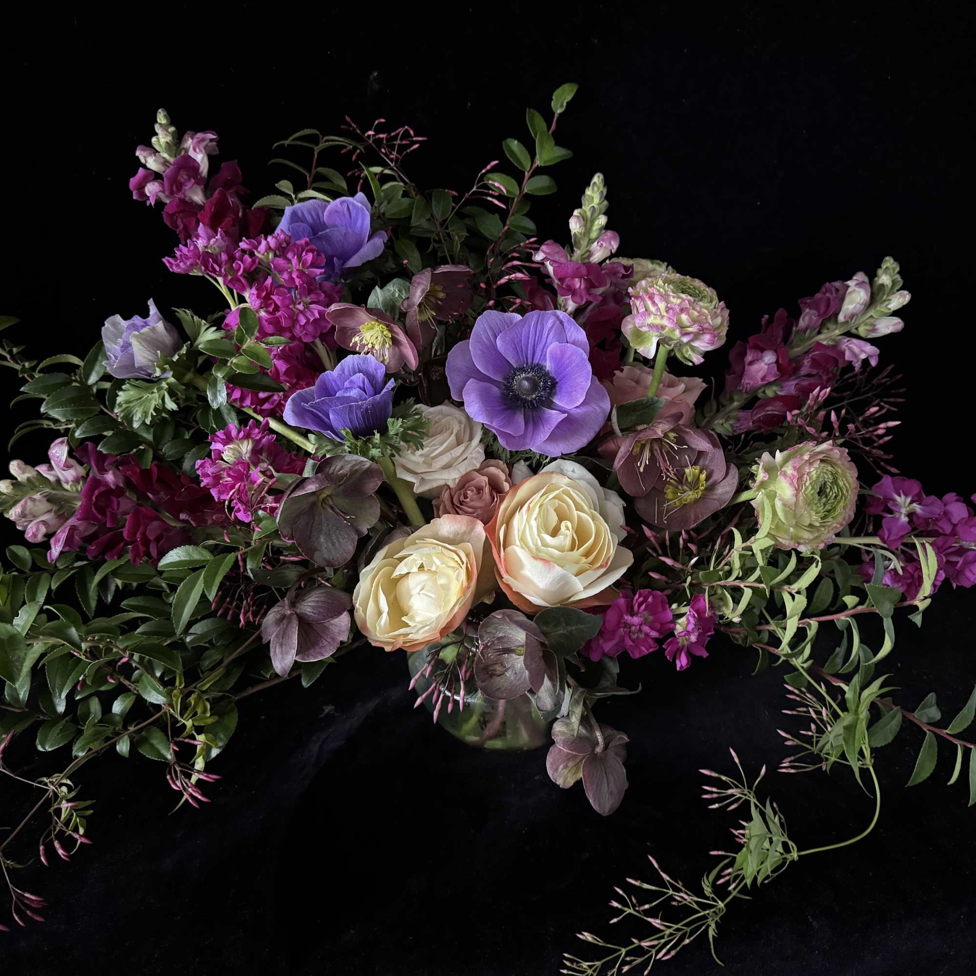 Bouquet of purple and cream flowers with trailing greenery on a black background