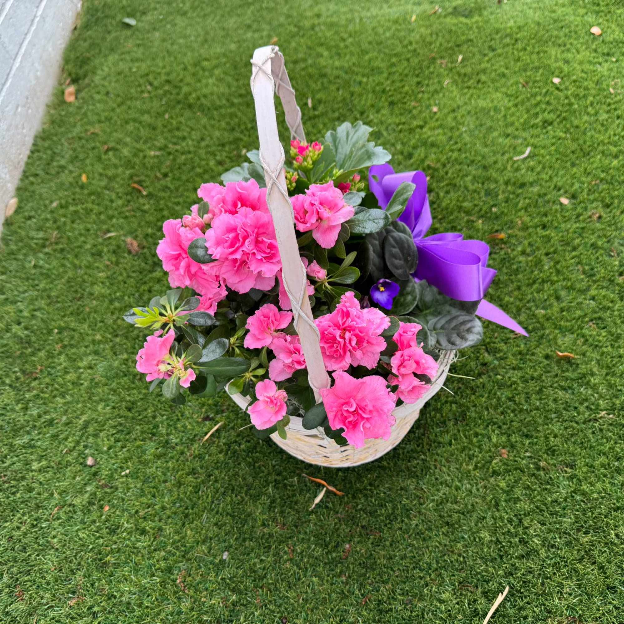 Pink flowers in a wicker basket with a purple ribbon