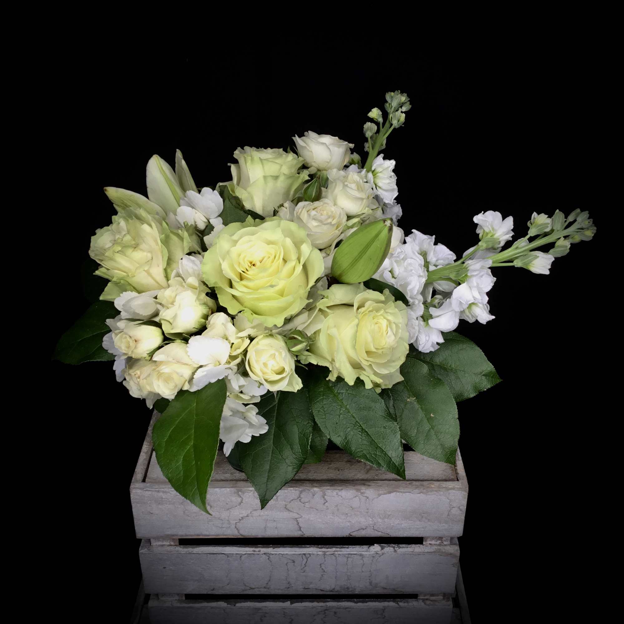 Pale yellow roses and white flowers arranged in a wooden crate