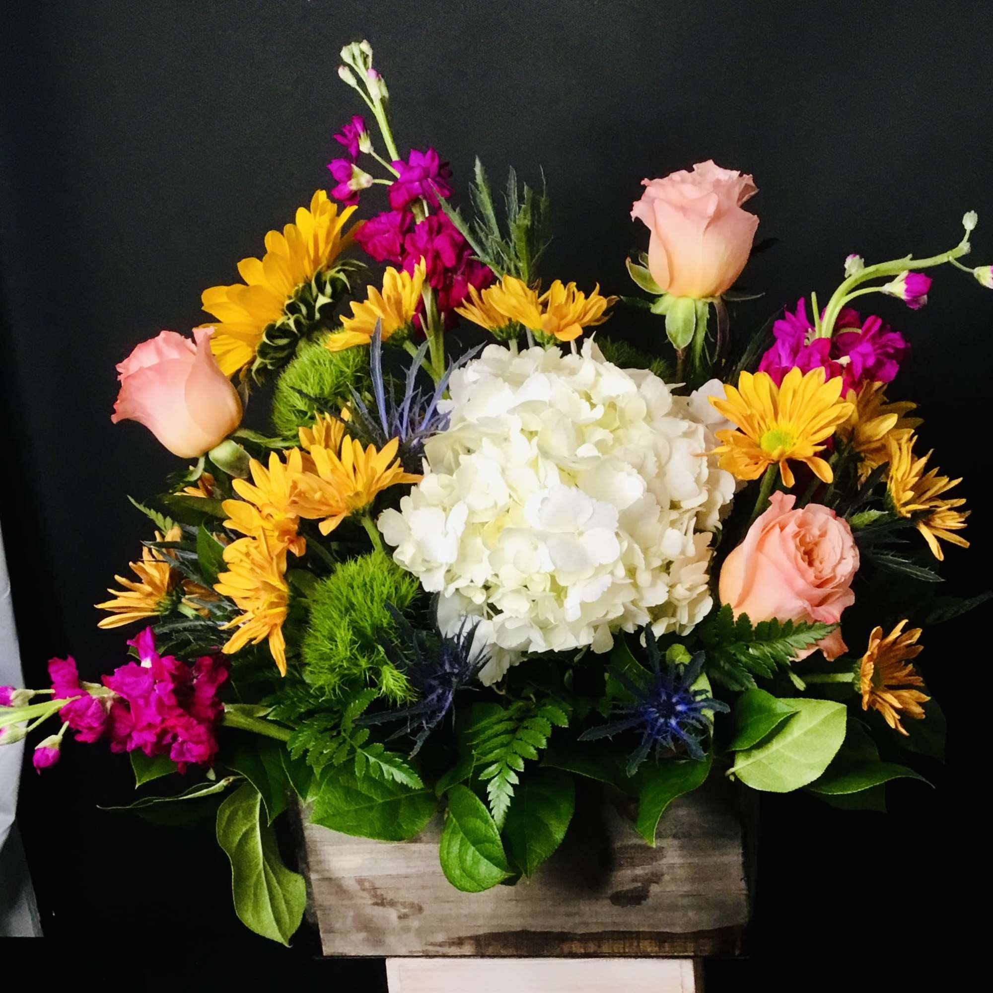 Mixed bouquet with white hydrangea, pink roses, and yellow daisies in a wooden box