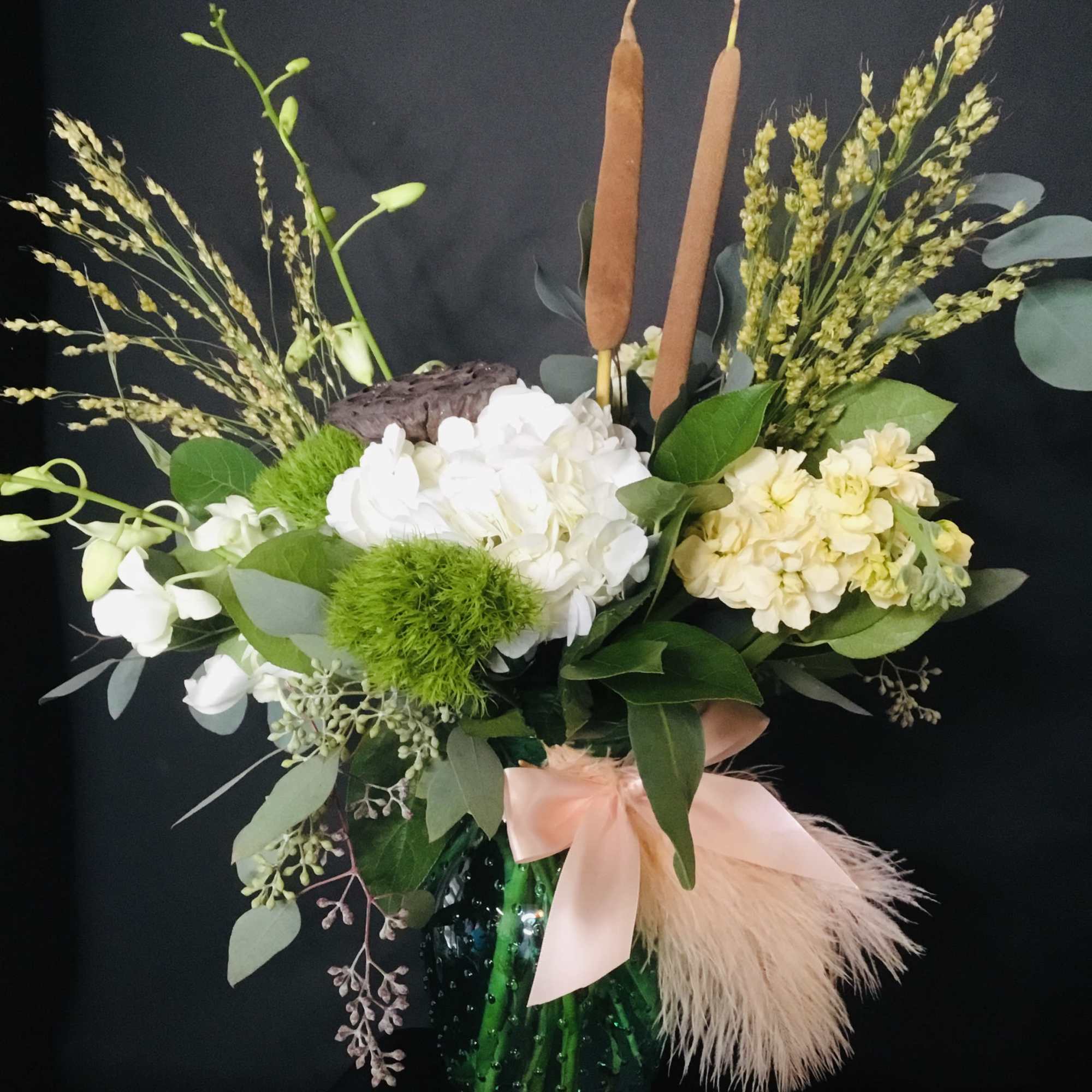 White and cream floral arrangement in a green vase with a pink ribbon