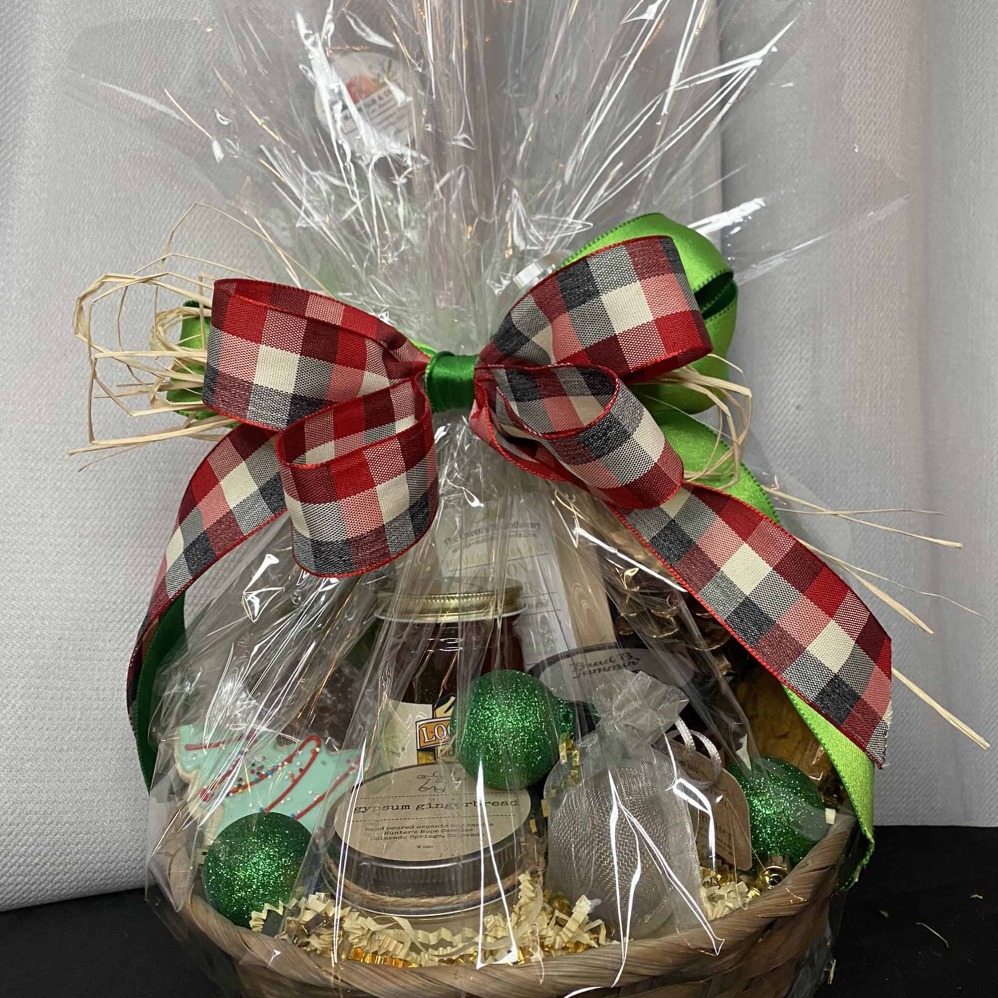 Gift basket with bottles and jars wrapped in clear cellophane and a plaid bow
