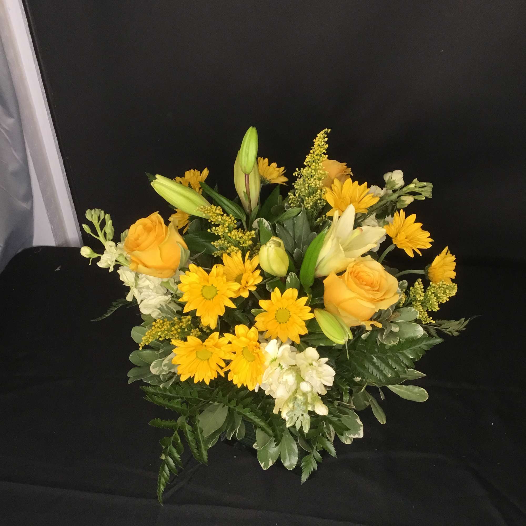 Yellow roses and daisies arranged with white lilies in a low bouquet