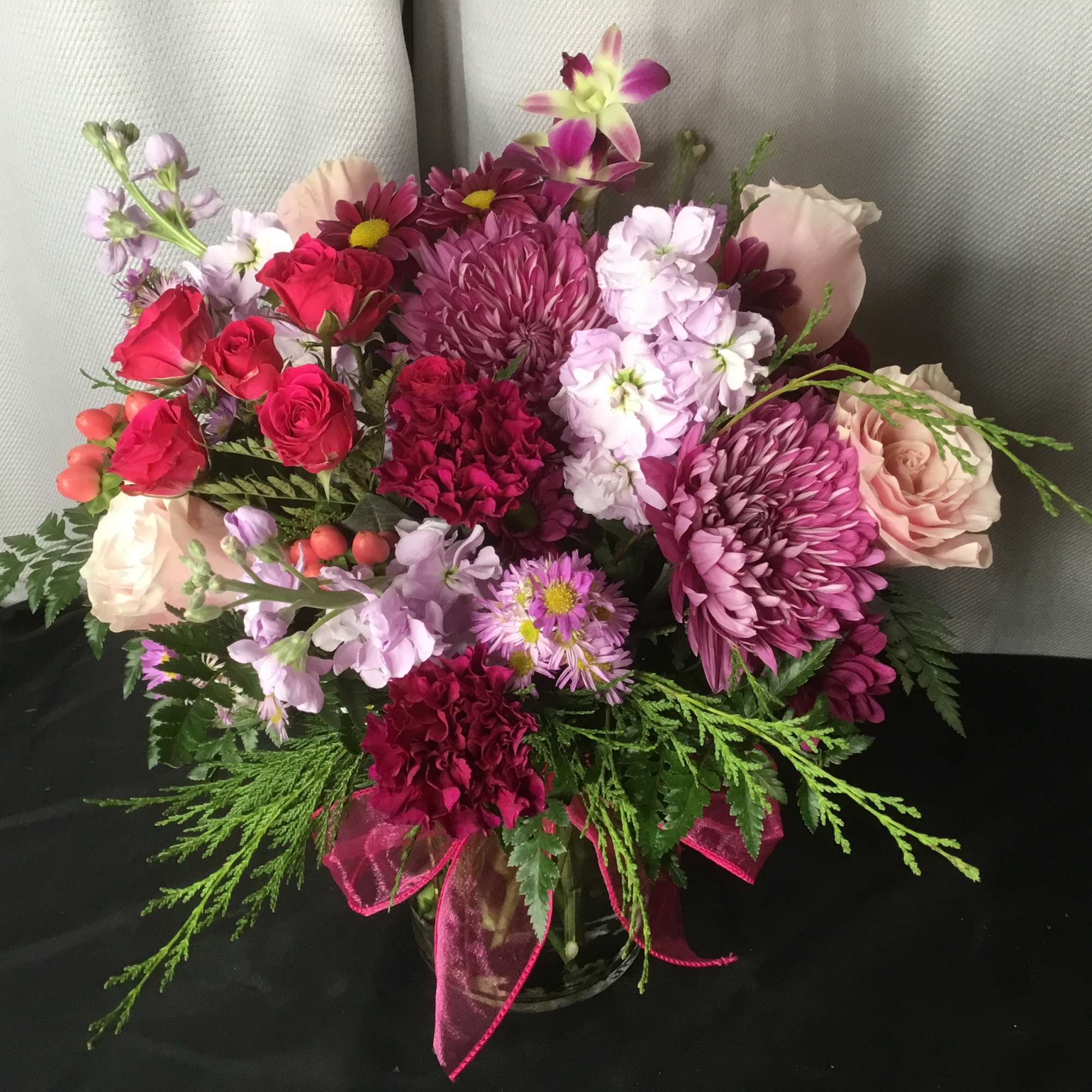 Mixed bouquet of pink, red, and lavender flowers in a glass vase with ribbon