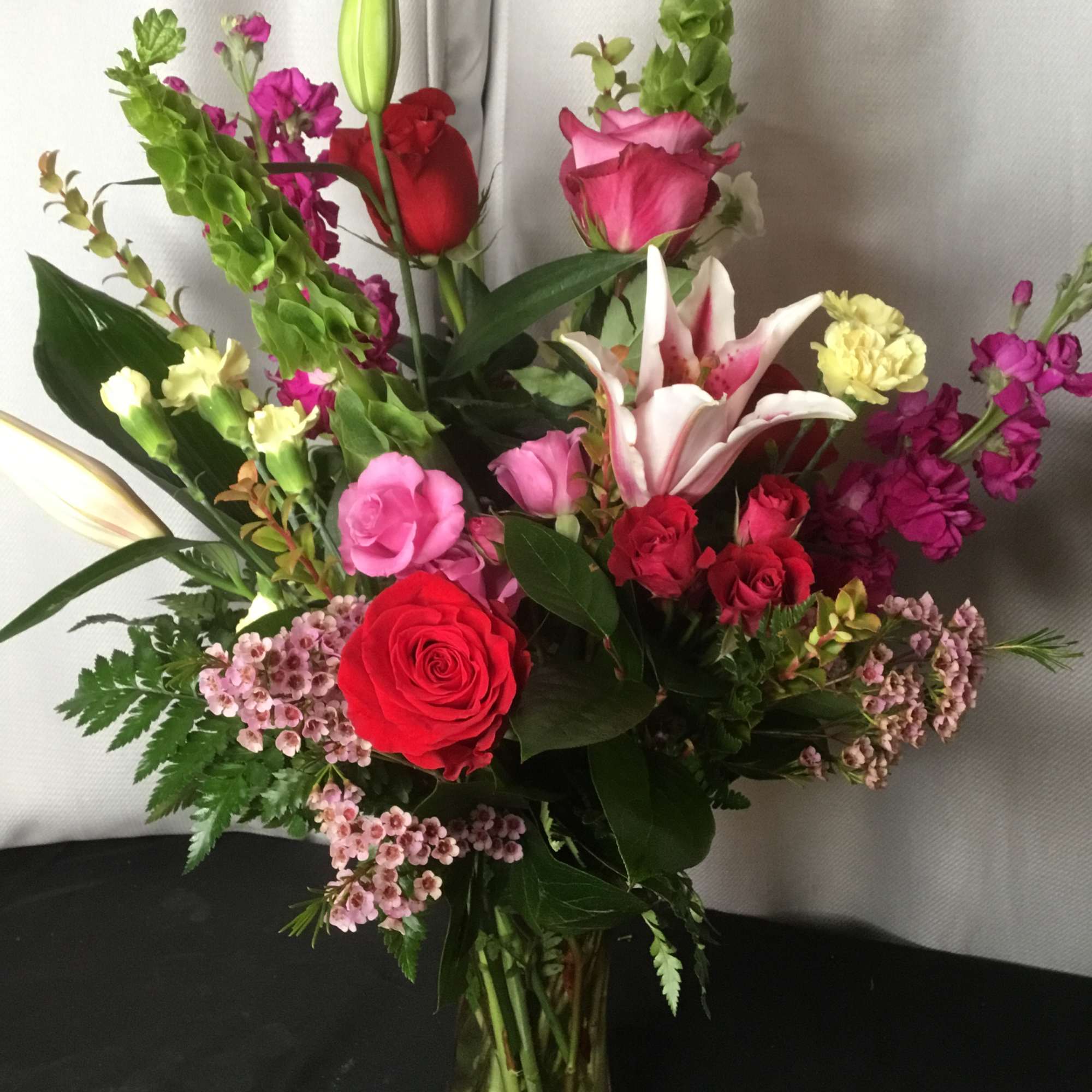 Mixed bouquet of roses, lilies, and pink filler flowers in a glass vase