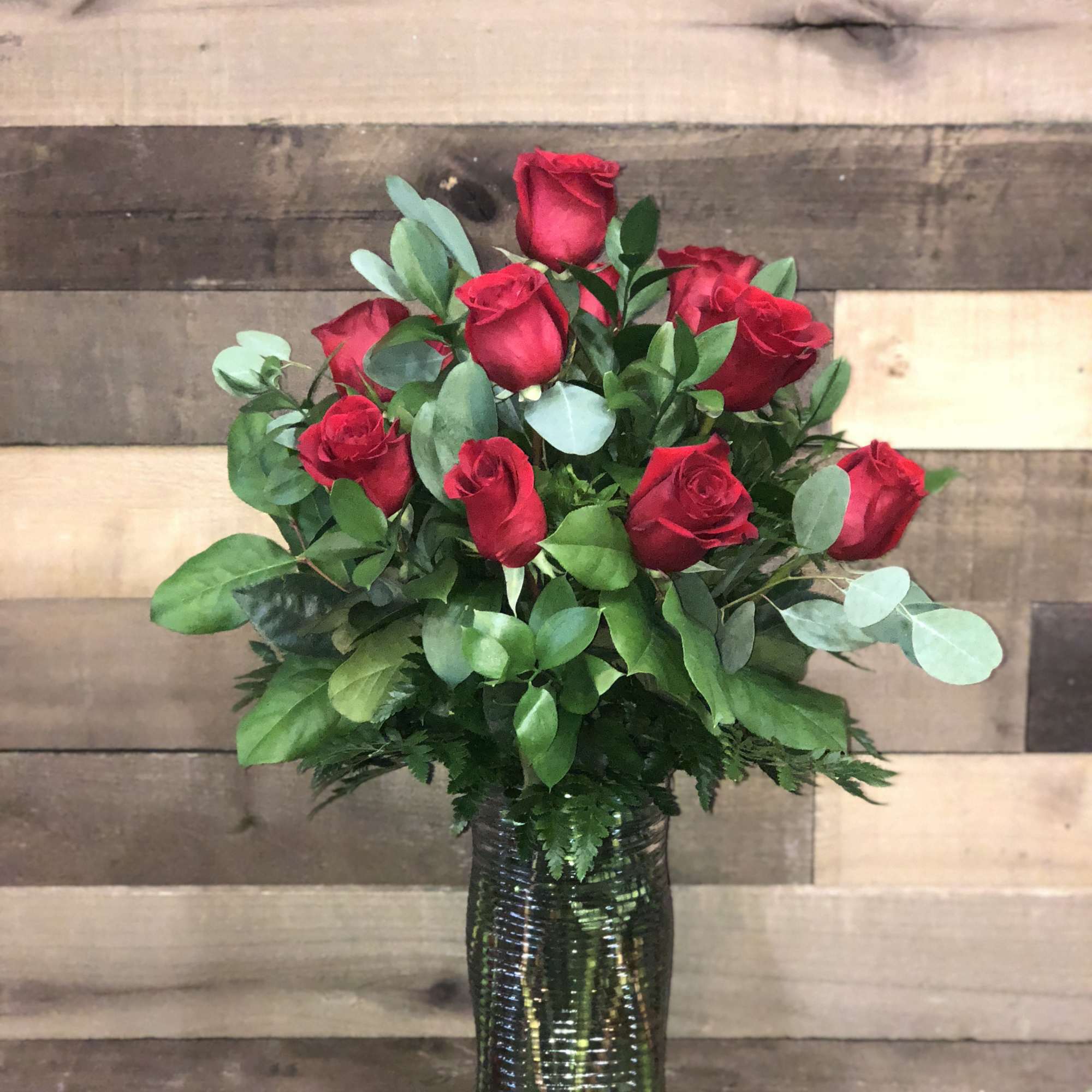 Red roses arranged in a tall glass vase with greenery