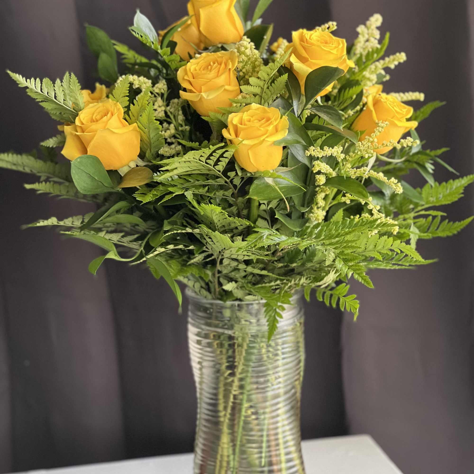 Yellow roses arranged in a clear glass vase with greenery