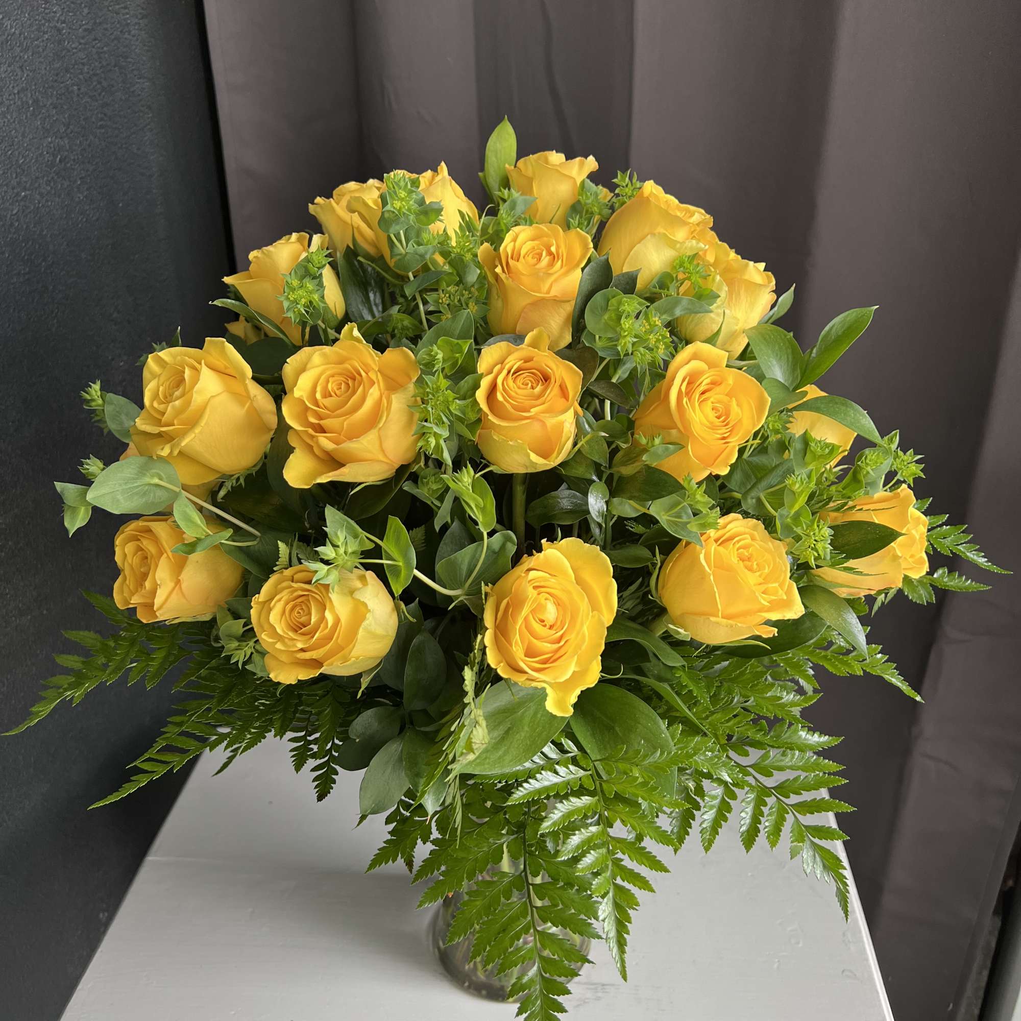 Yellow roses arranged in a clear glass vase with greenery
