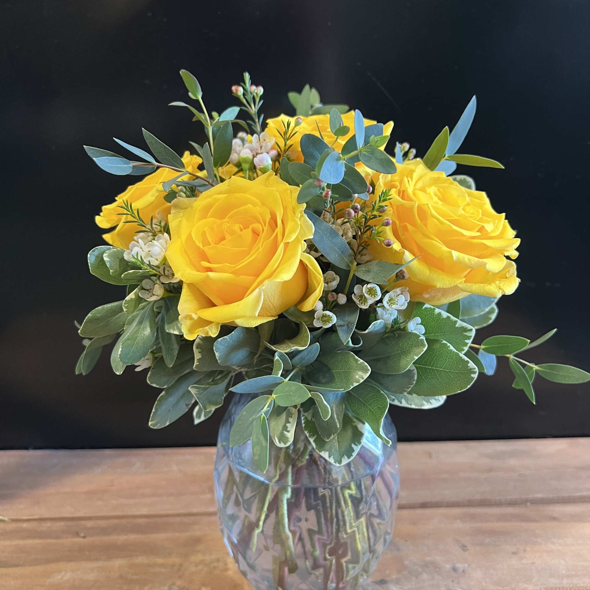 Yellow roses arranged in a clear glass vase with mixed greenery
