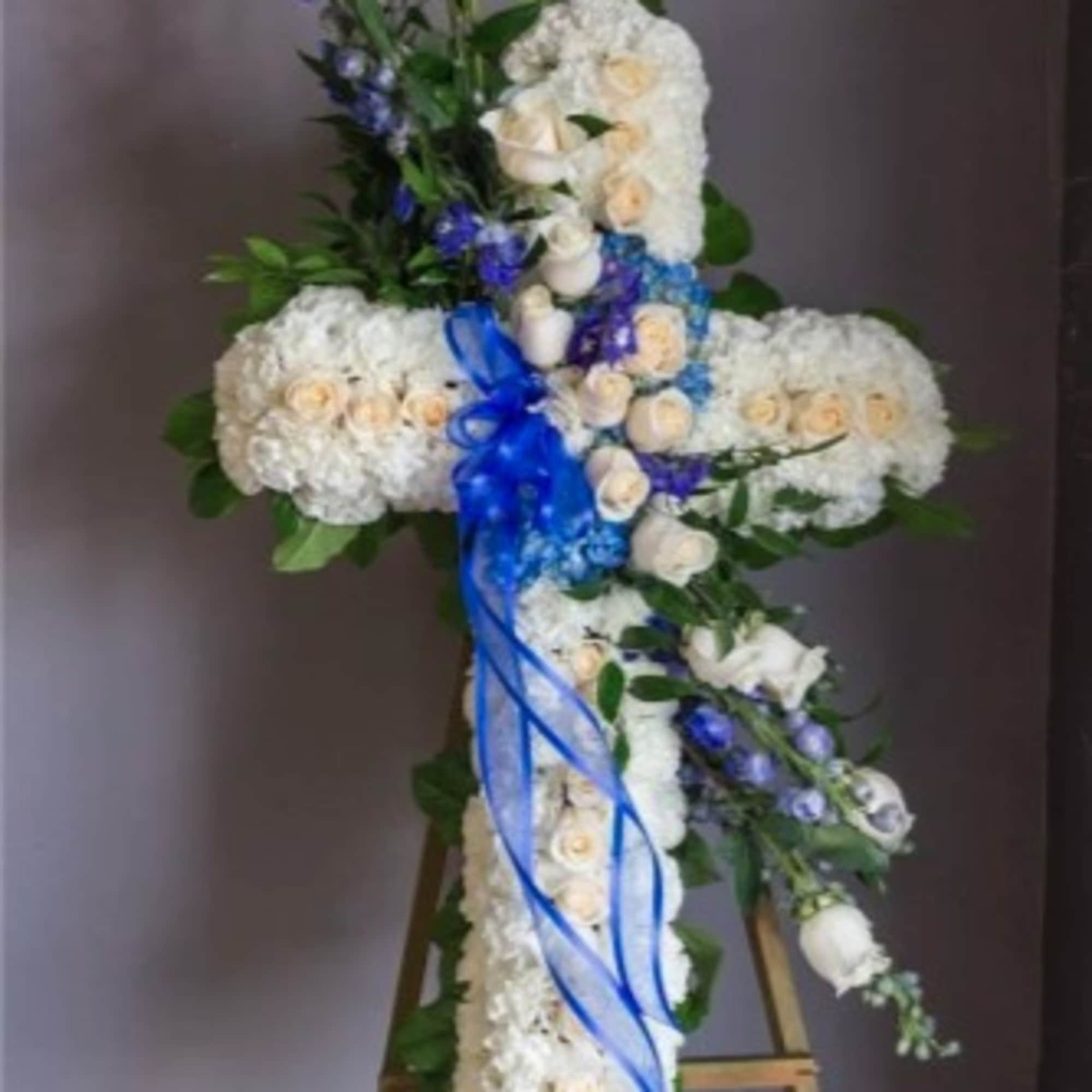 Tall floral cross arrangement with white roses and blue ribbon