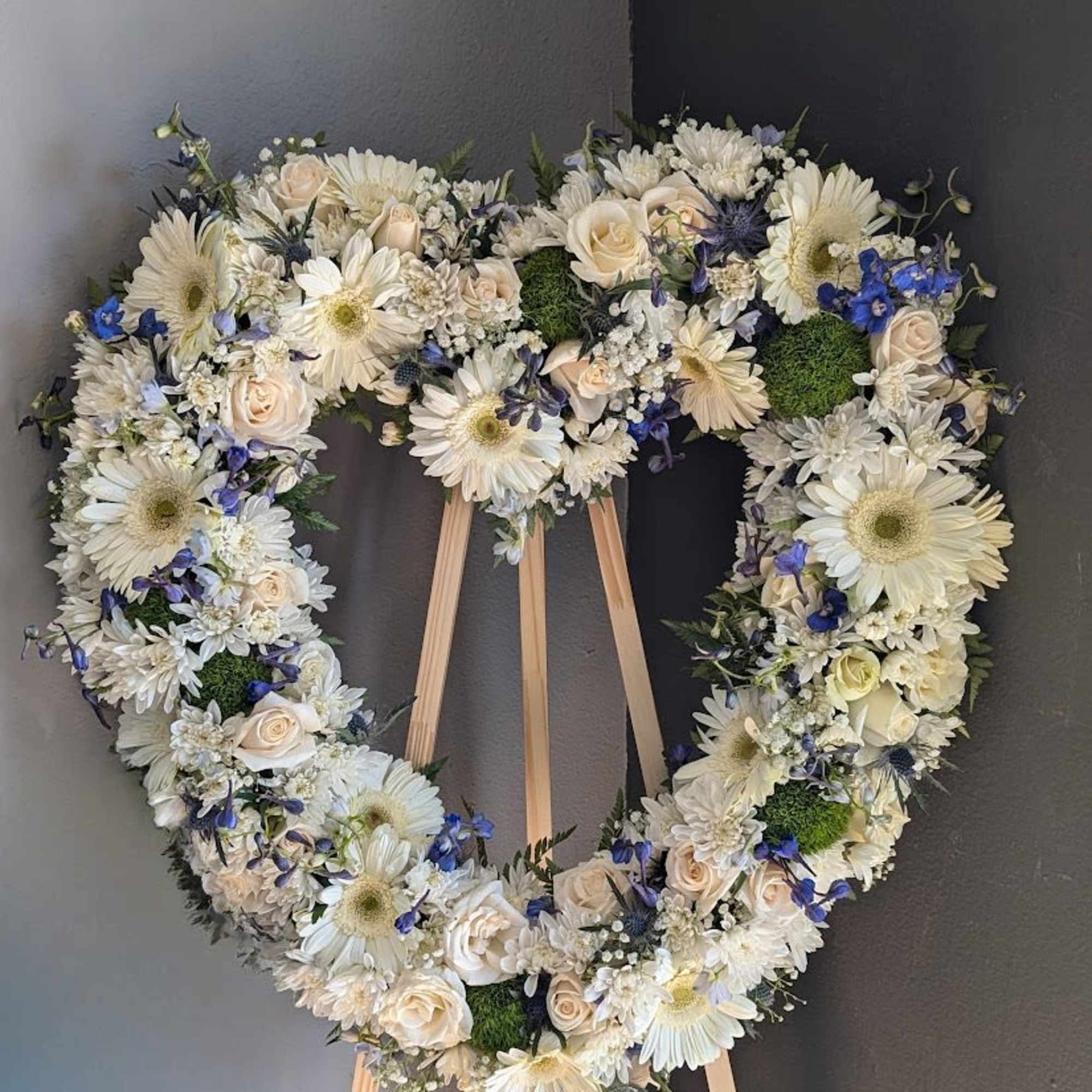 Heart-shaped floral wreath on a wooden stand with white and blue flowers