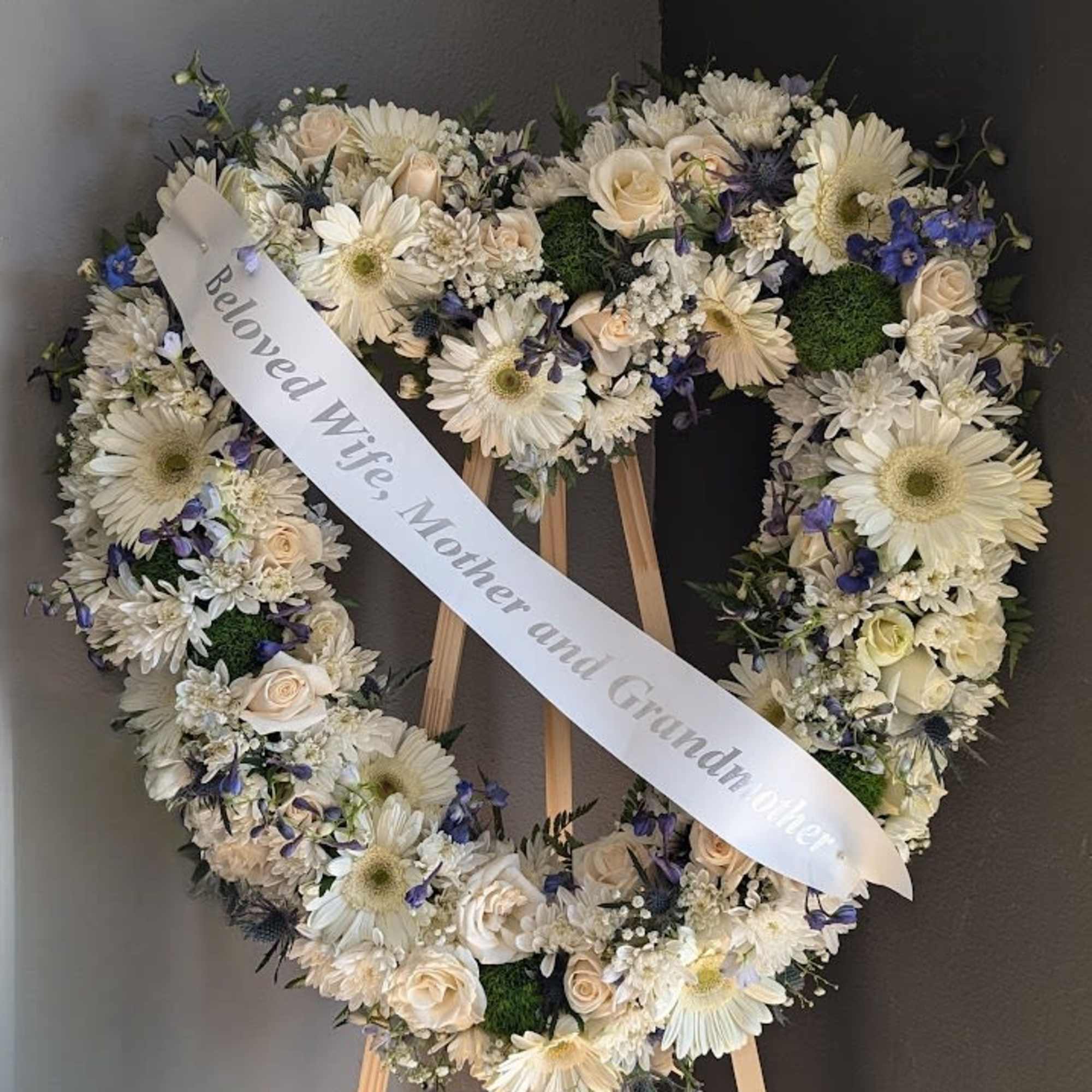 Heart-shaped white floral wreath on an easel with a memorial ribbon