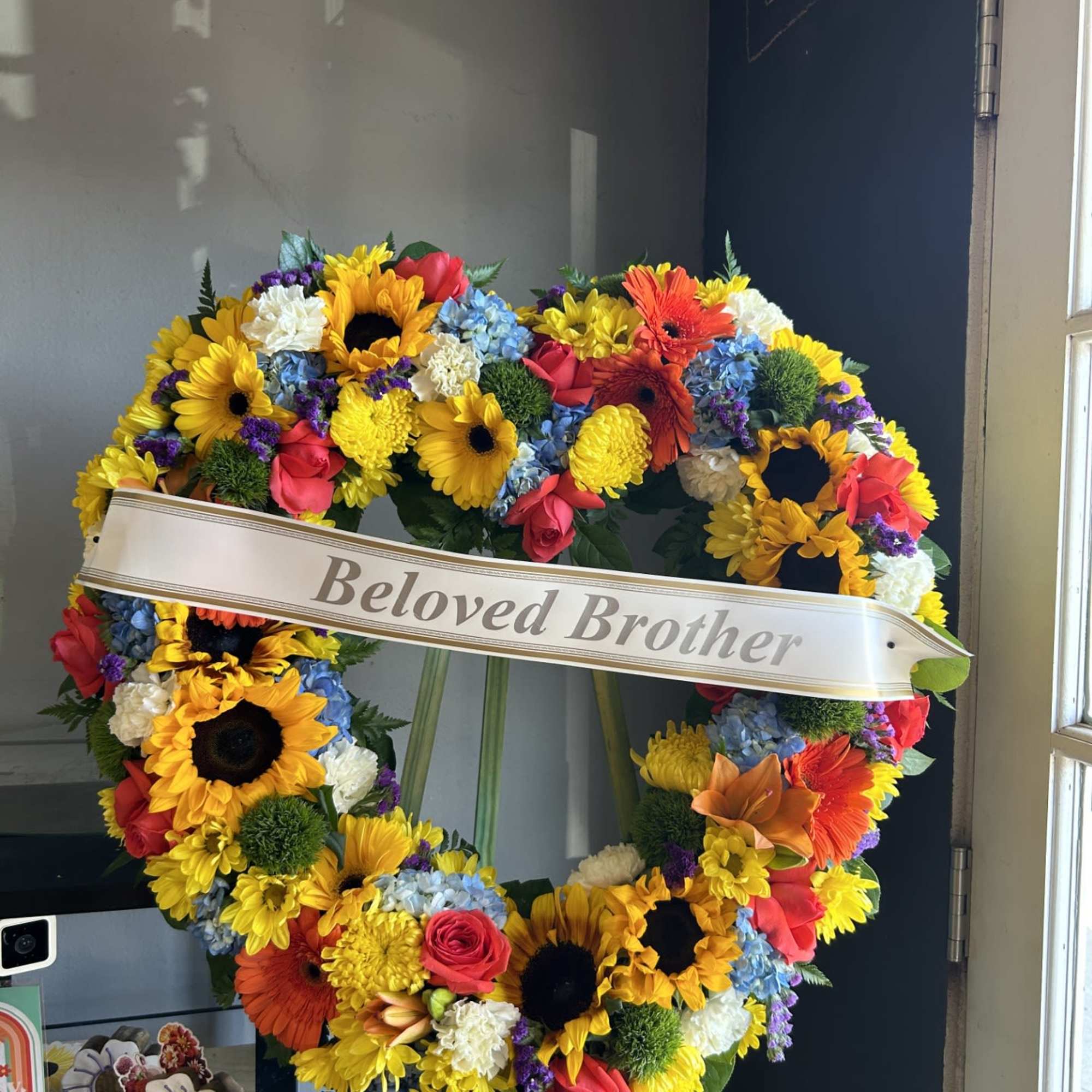 Heart-shaped funeral wreath with colorful flowers and a "Beloved Brother" ribbon