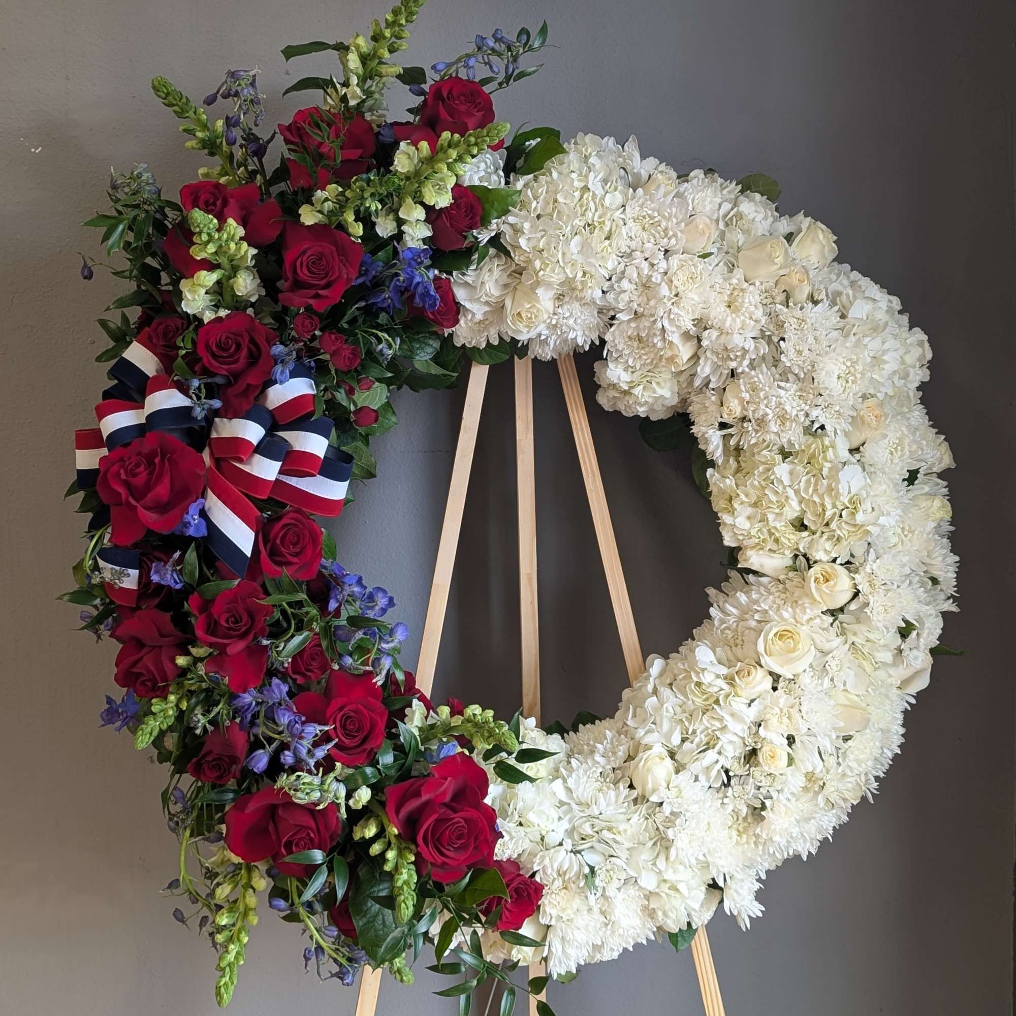 Circular floral wreath with red roses and white blooms on a wooden easel