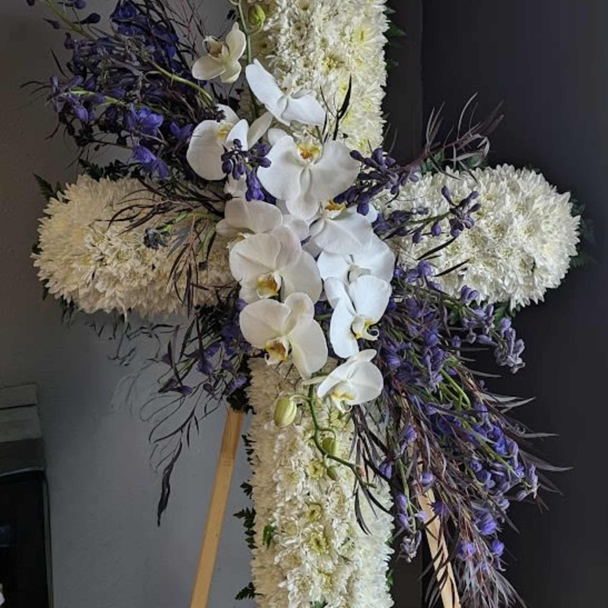 White floral cross on an easel with purple accents and orchids