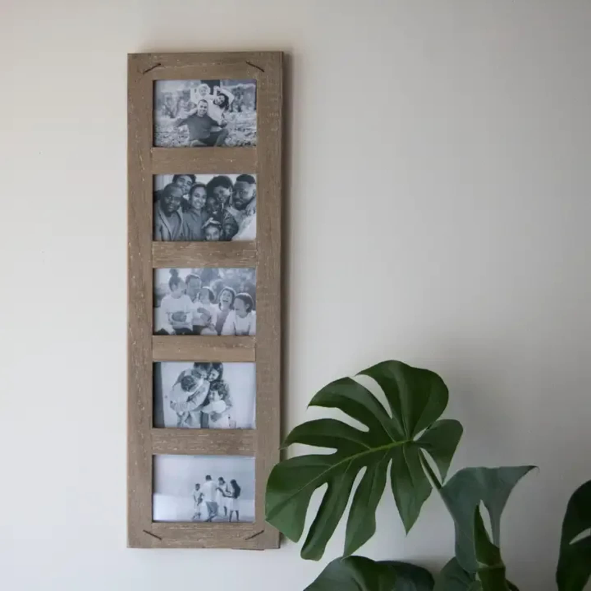 Wooden wall photo frame with five black-and-white pictures beside a large green leaf