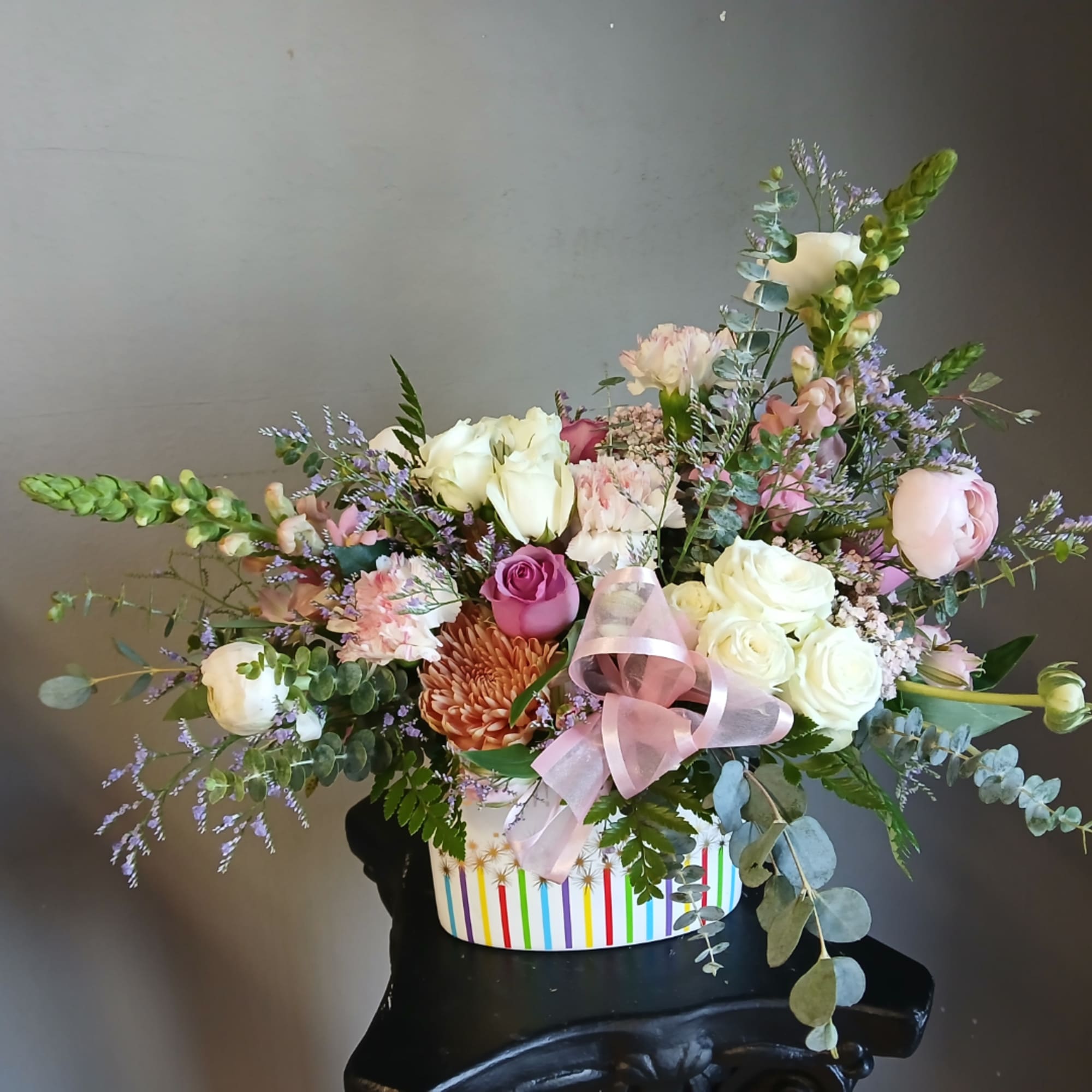 Mixed bouquet of roses, chrysanthemums, and pastel flowers in a striped box
