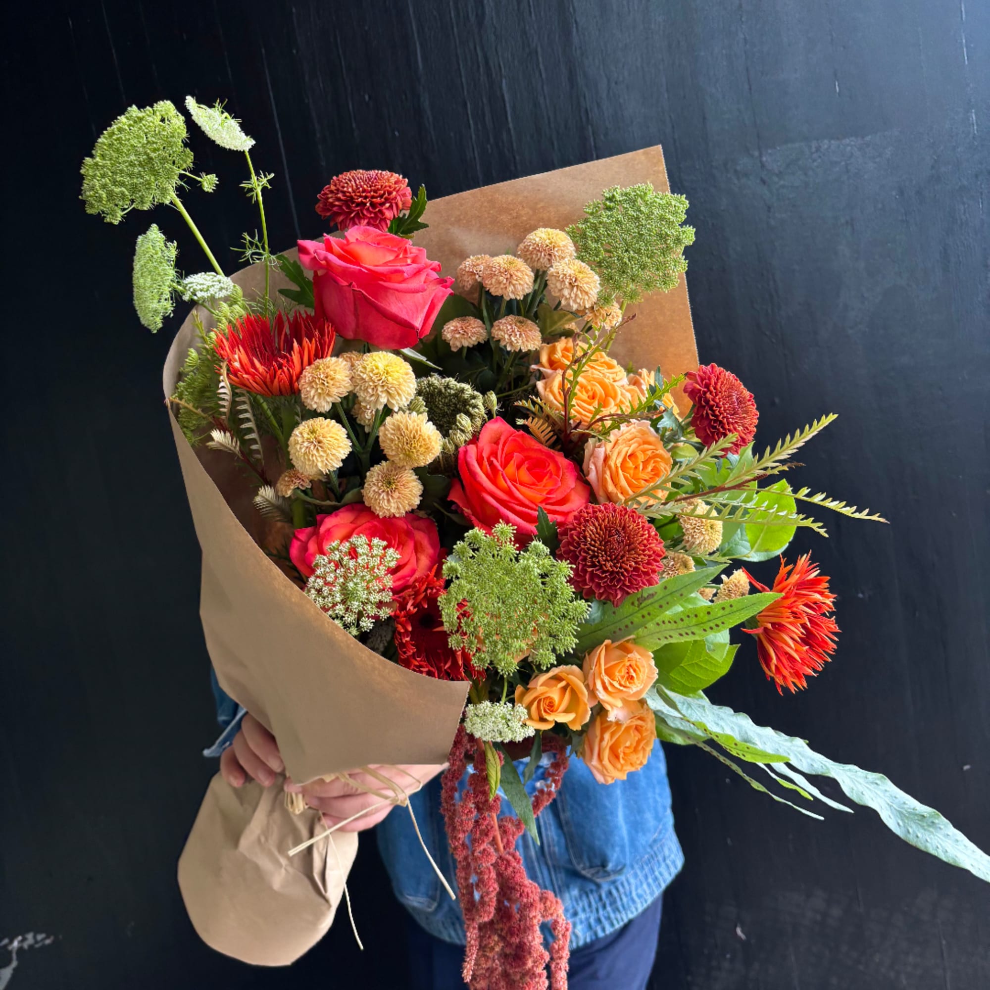 Mixed bouquet of roses, chrysanthemums, and orange blooms wrapped in kraft paper
