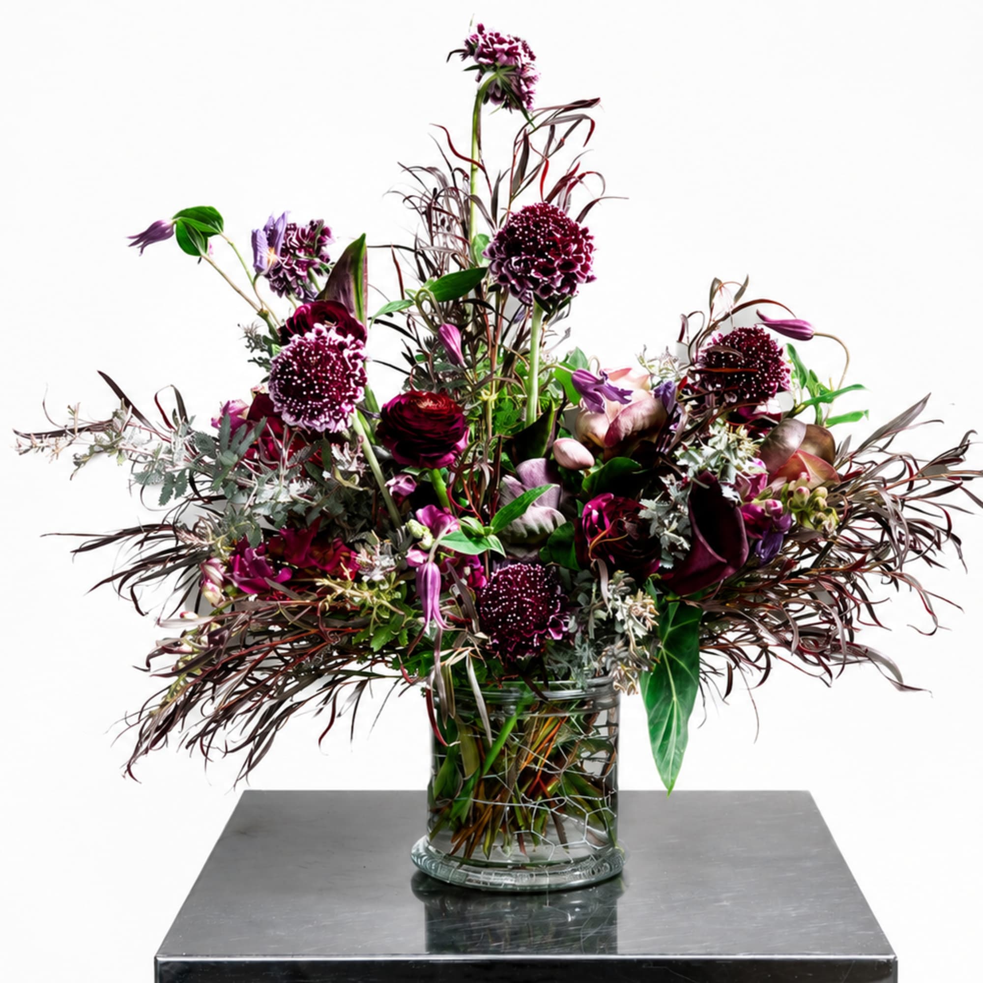 Tall burgundy and purple floral arrangement in a clear glass vase