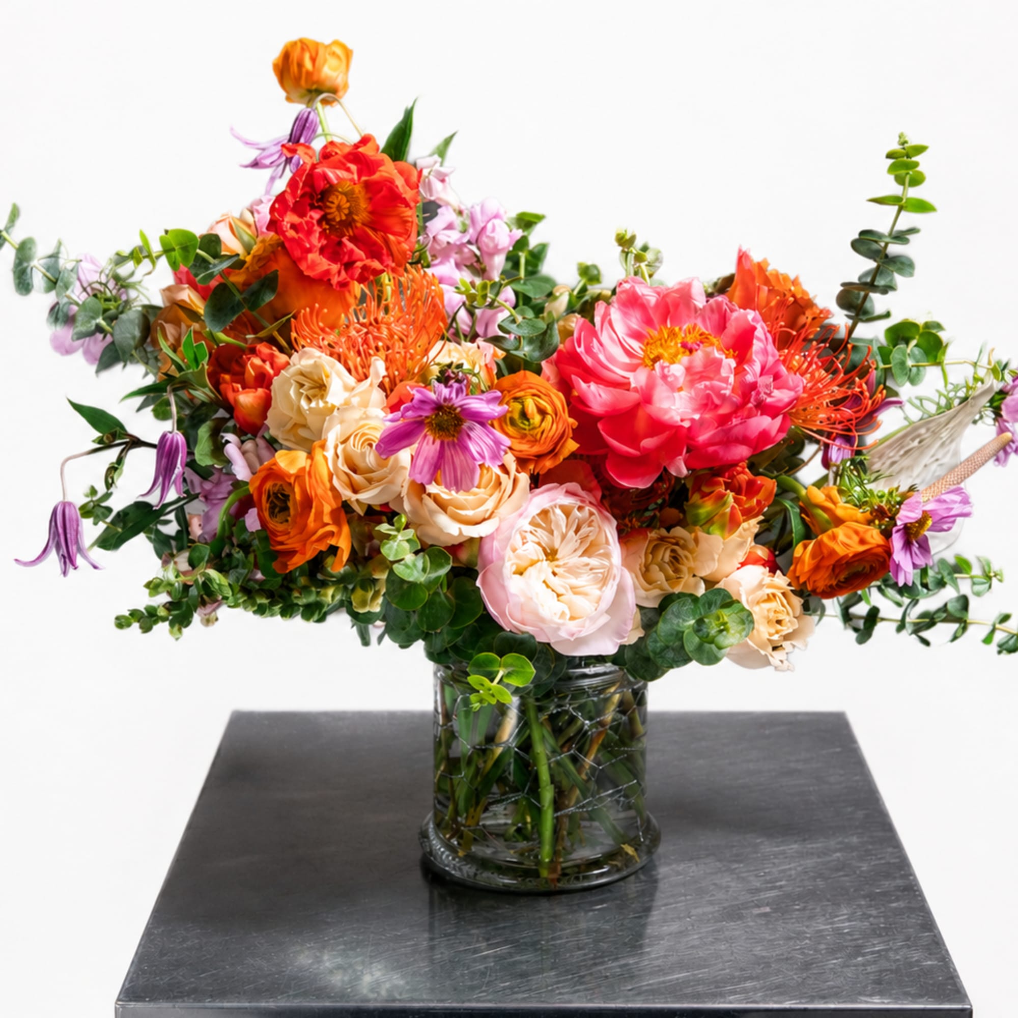 Mixed bouquet of orange, pink, and purple flowers in a glass vase