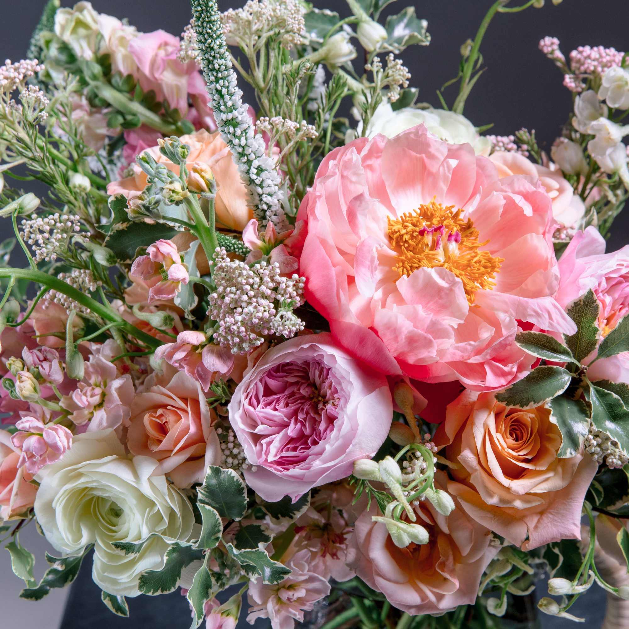 Soft, garden-fresh blooms spill from a dark glass pitcher vase to create