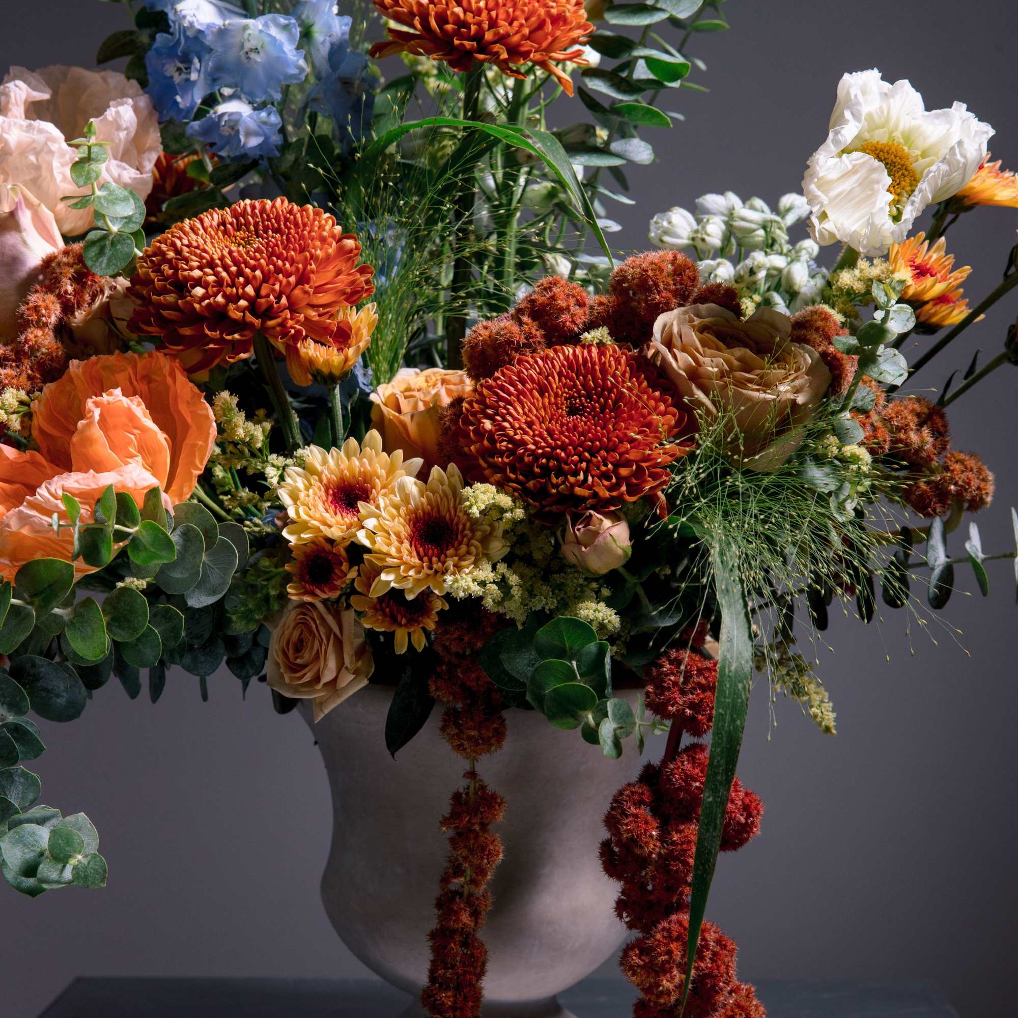 Tall sky-blue delphinium towers over a lush cluster of vivid orange chrysanthemums