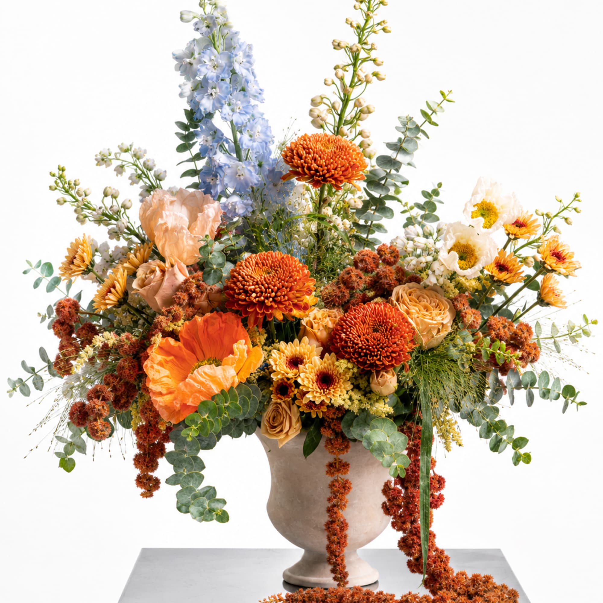 Large mixed floral arrangement in a beige vase with orange, blue, and cream blooms