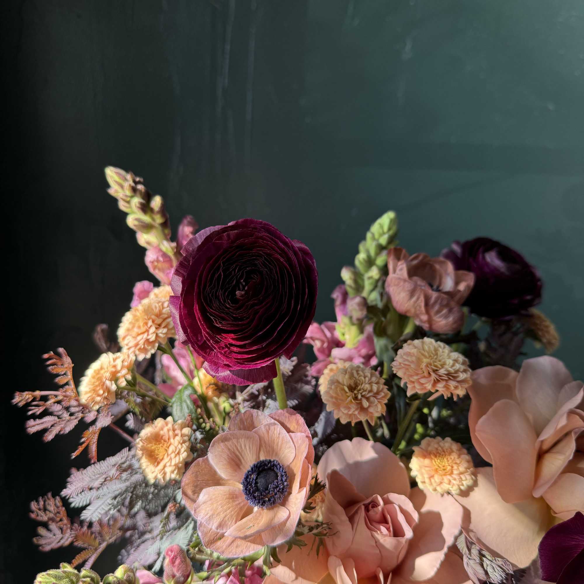 Bouquet of peach, pink, and burgundy flowers against a dark background