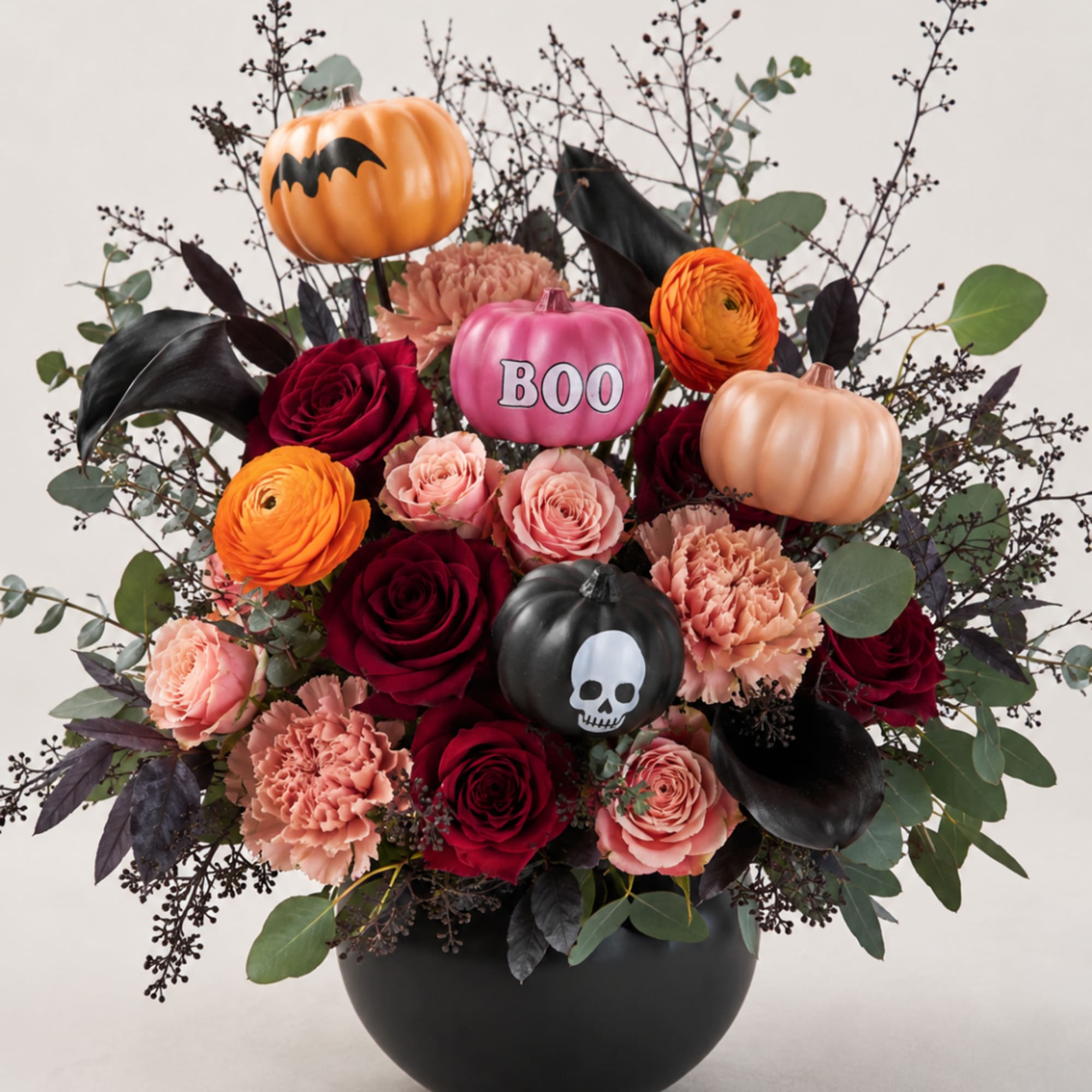 Halloween bouquet with roses, carnations, and pumpkin decorations in a black vase