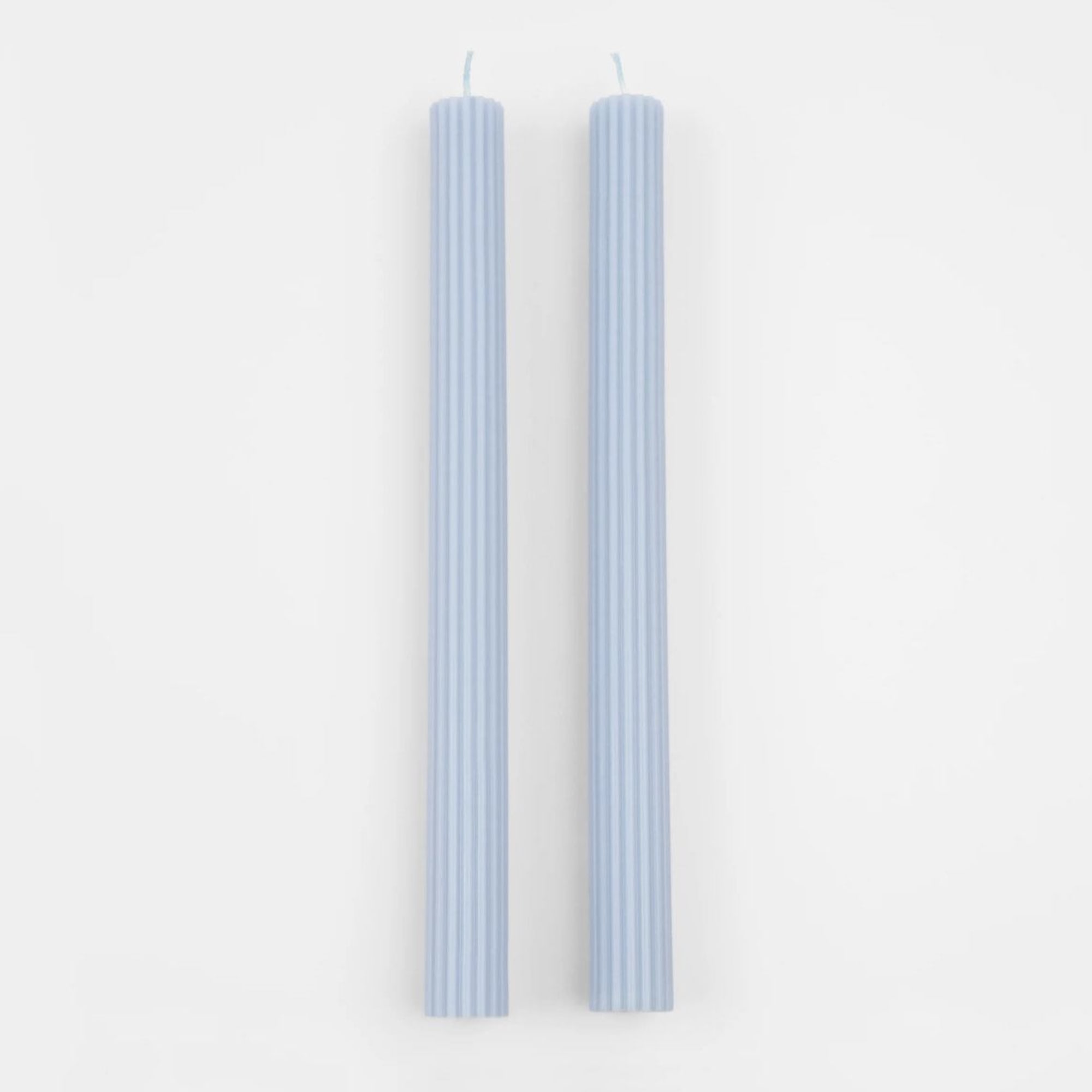 Two light blue ribbed taper candles on a white background