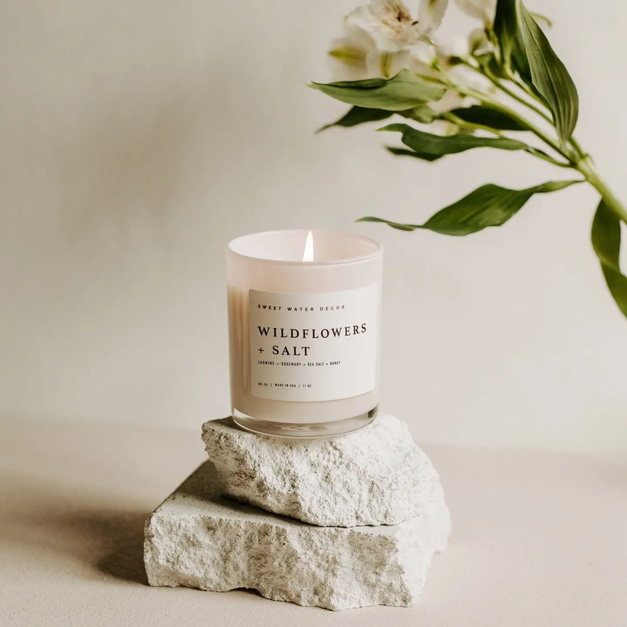 Lit candle in a glass jar on stacked stone blocks with a flower stem nearby