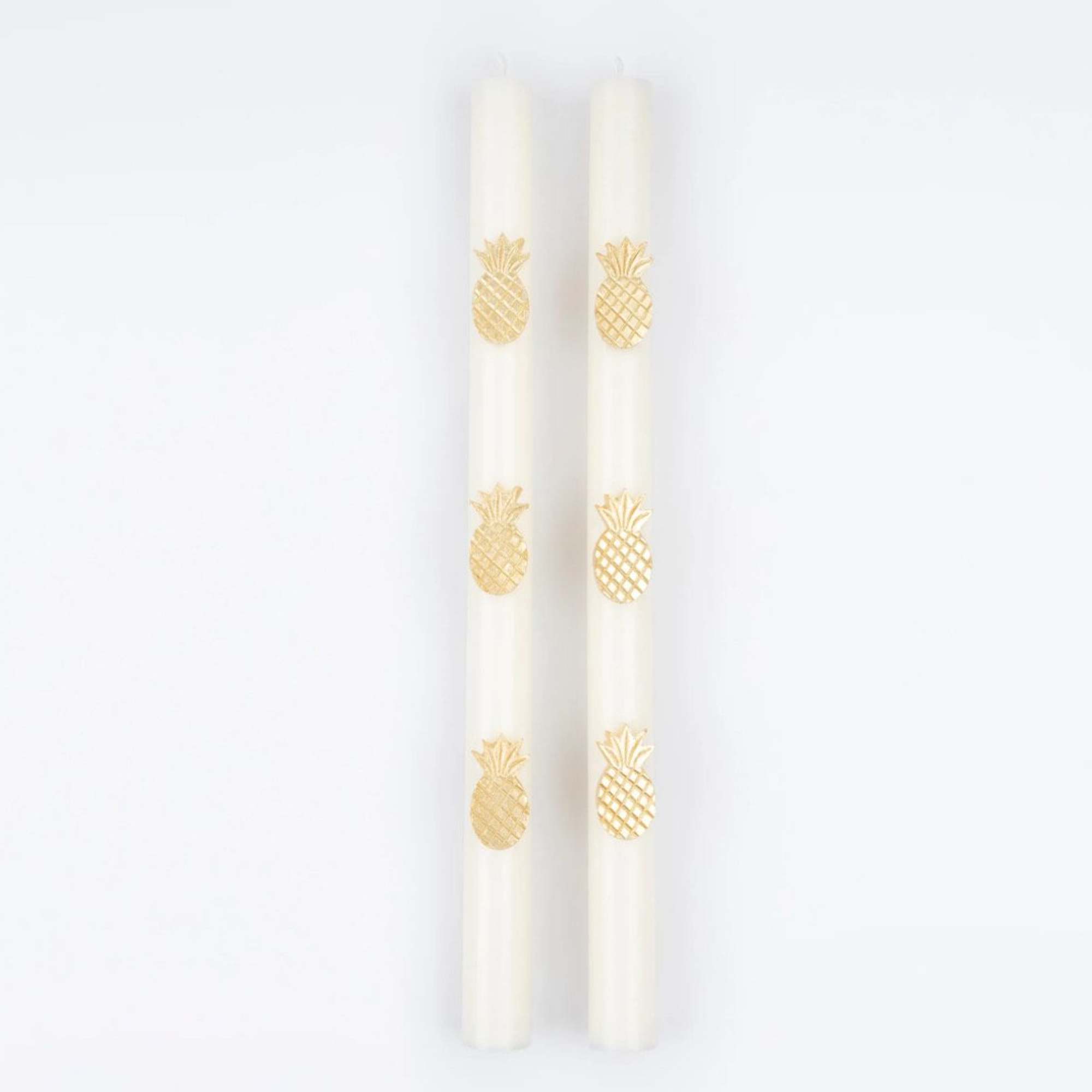 Two white taper candles with gold pineapple decorations