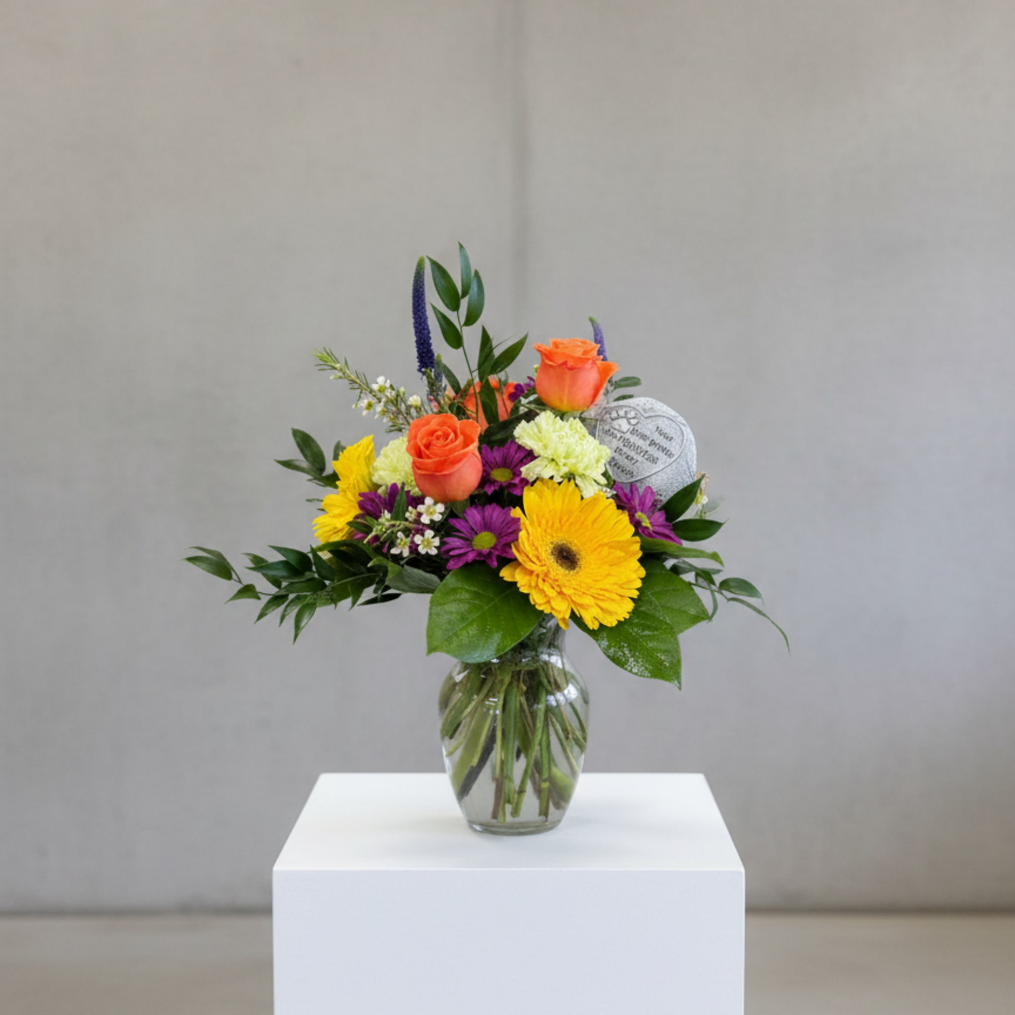 Mixed bouquet of orange roses, yellow gerberas, and purple daisies in a glass vase
