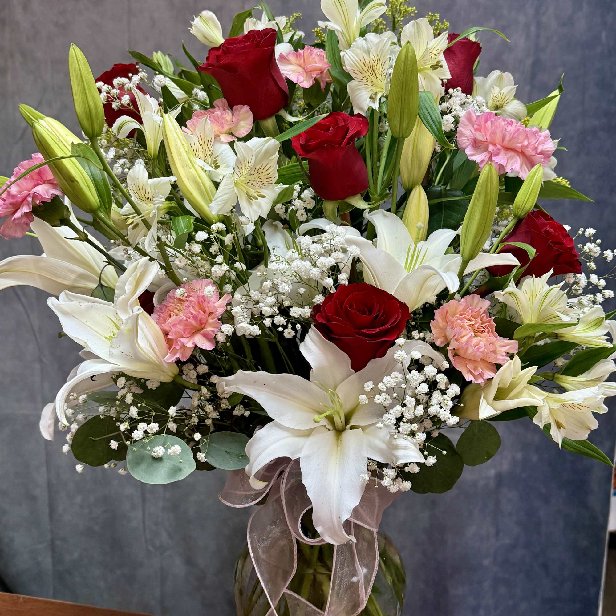 Bouquet of red roses, white lilies, and pink carnations in a glass vase