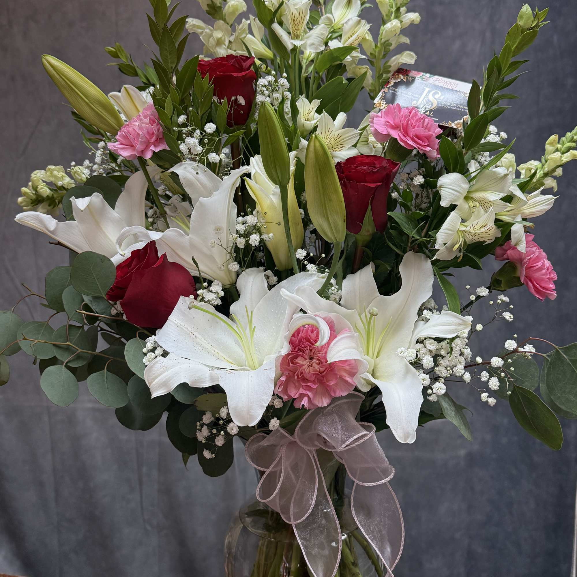 Bouquet of white lilies, red roses, and pink carnations in a glass vase