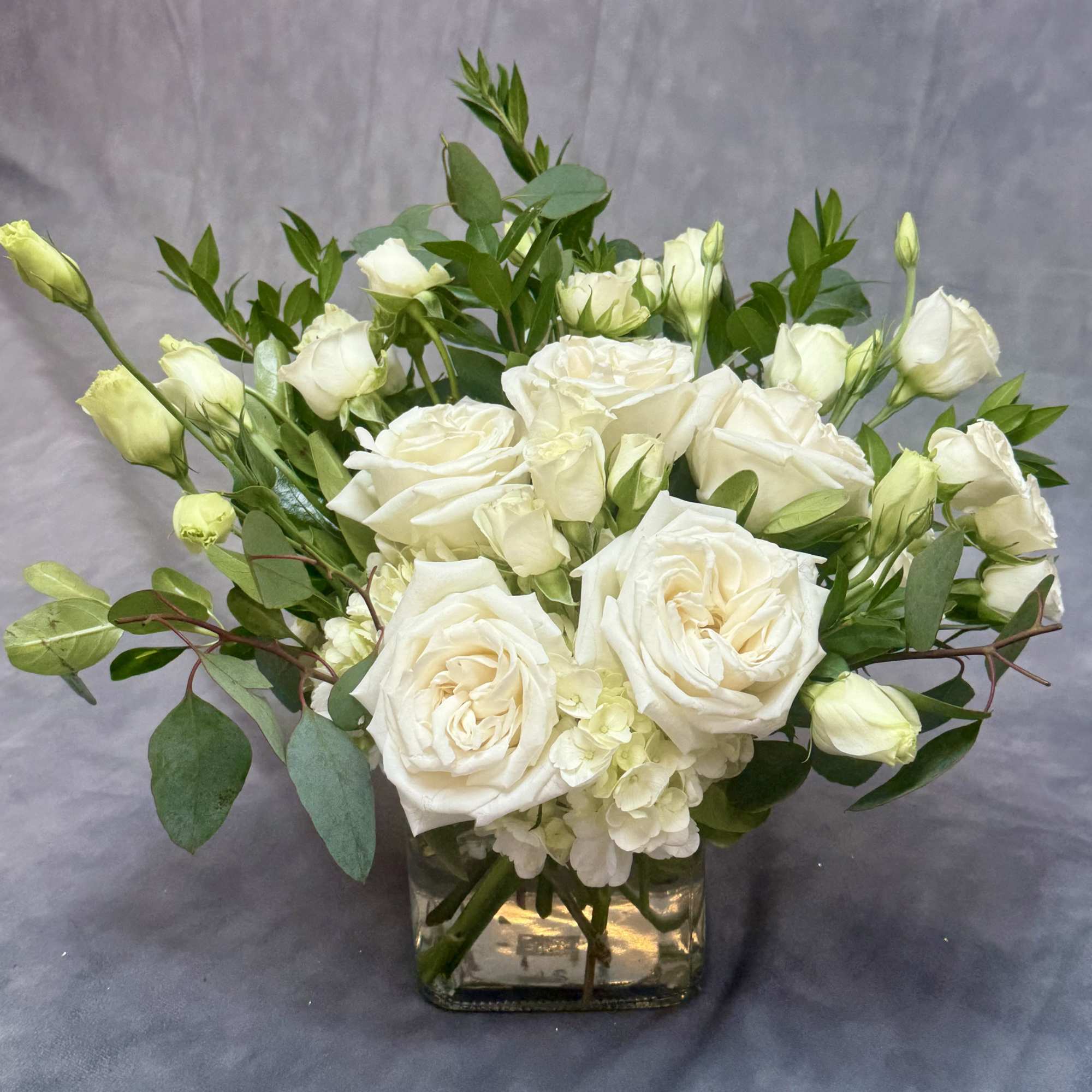White roses and buds arranged in a square glass vase