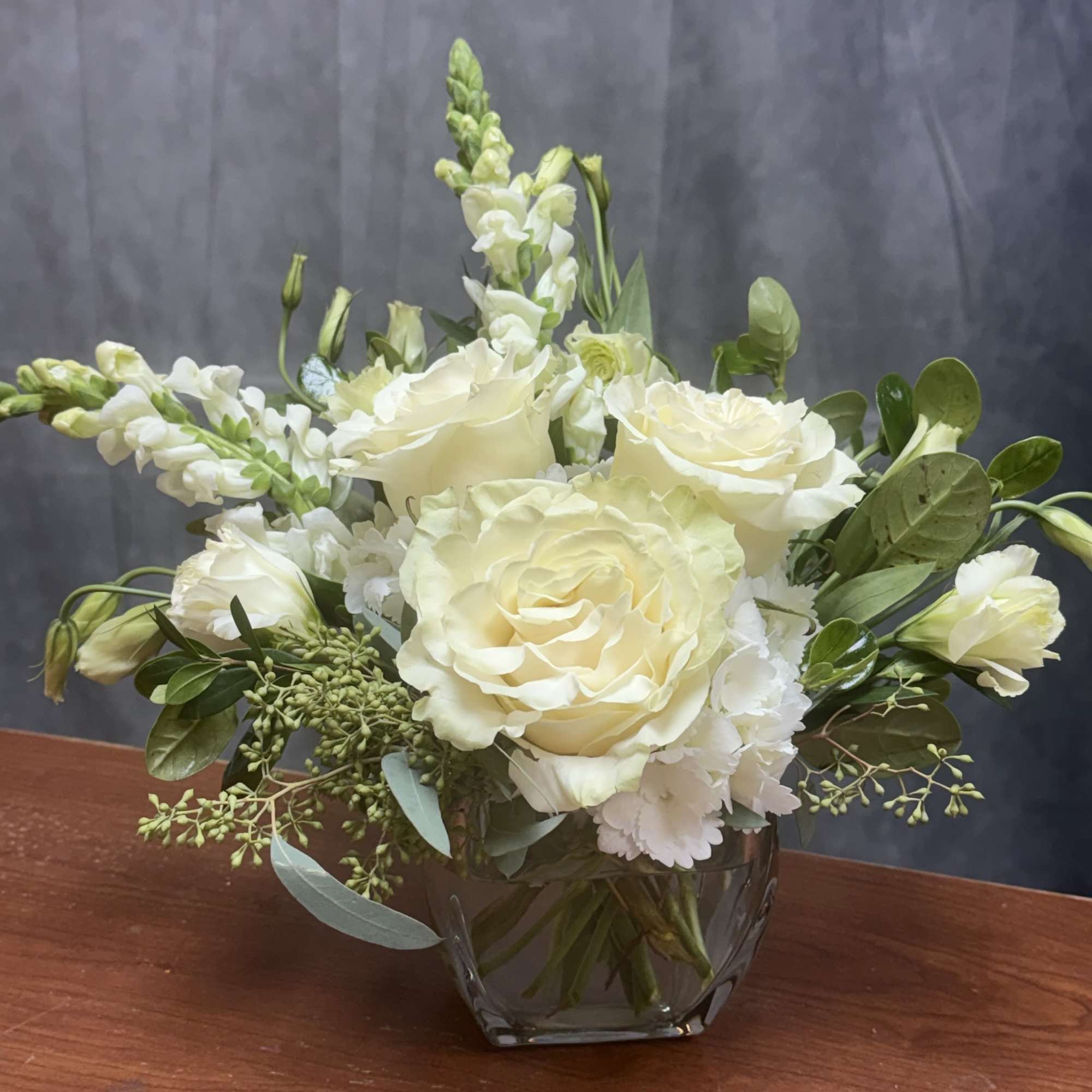 Cream roses and white snapdragons arranged in a glass vase