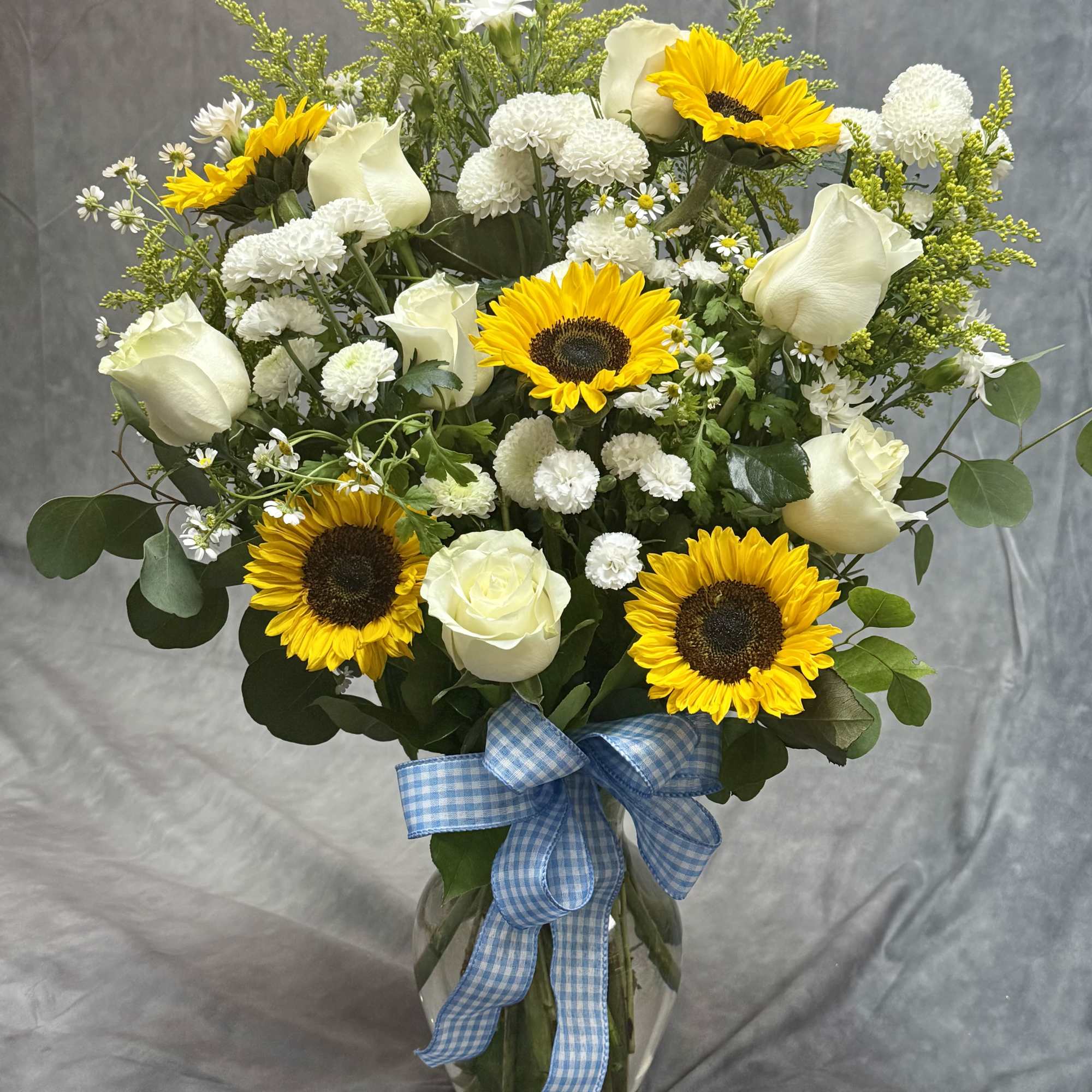 Bouquet of sunflowers and white roses in a glass vase with a blue ribbon