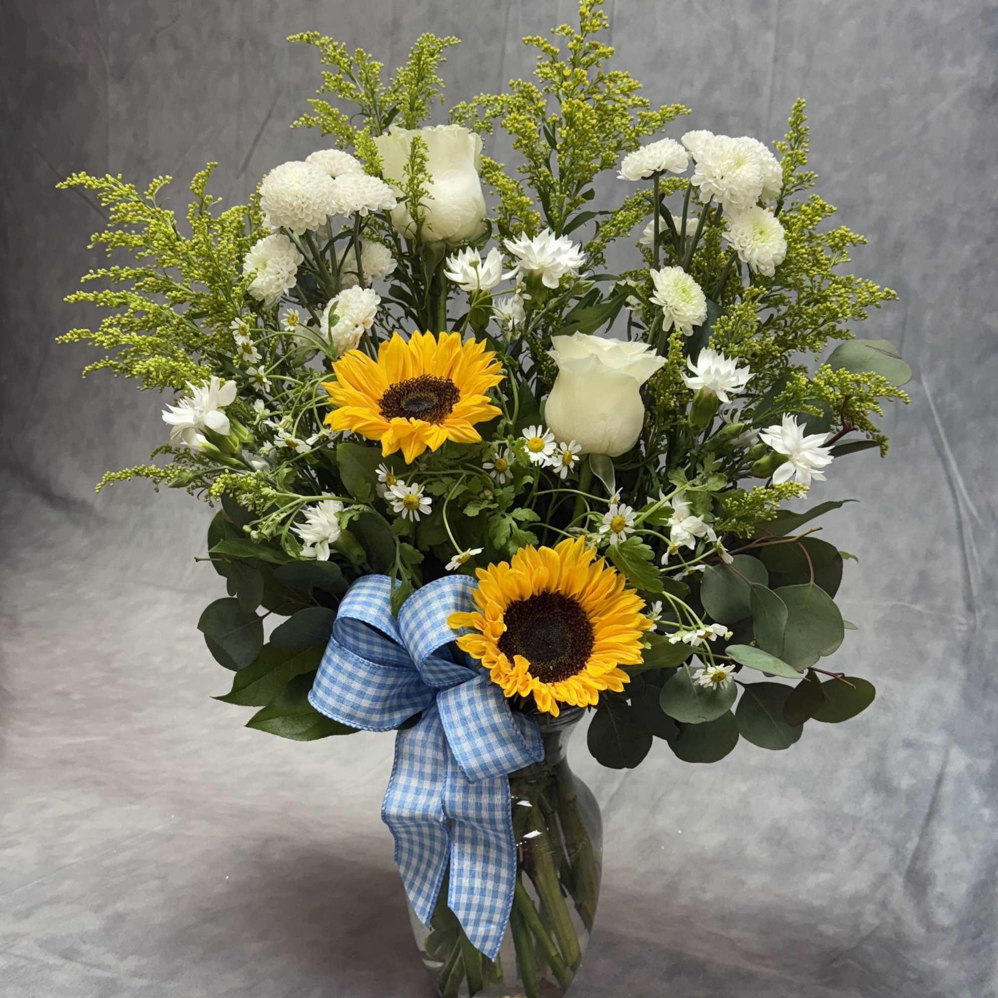 Sunflower and white rose bouquet in a glass vase with a blue ribbon