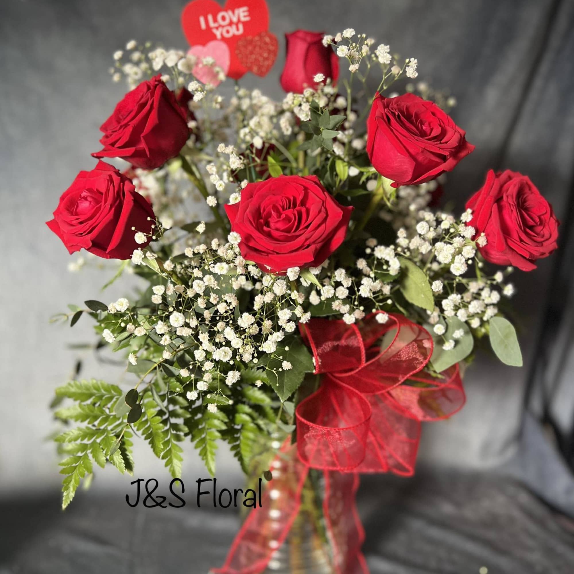 Red roses in a glass vase with baby's breath and a red ribbon