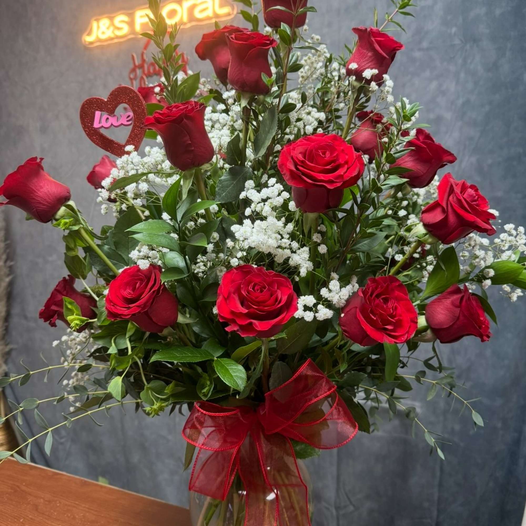 Red roses in a glass vase with baby's breath and a heart decoration